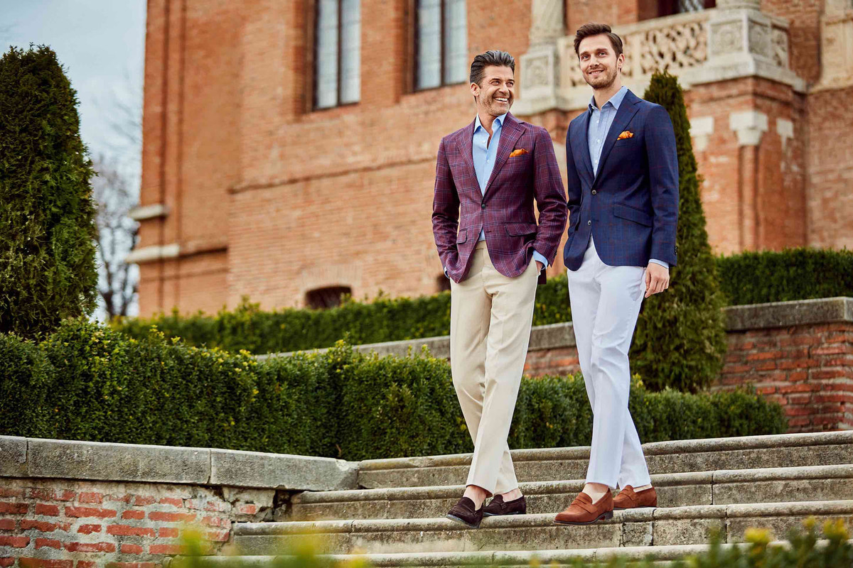 Two blazer ensembles with light trousers on the steps of a historic building