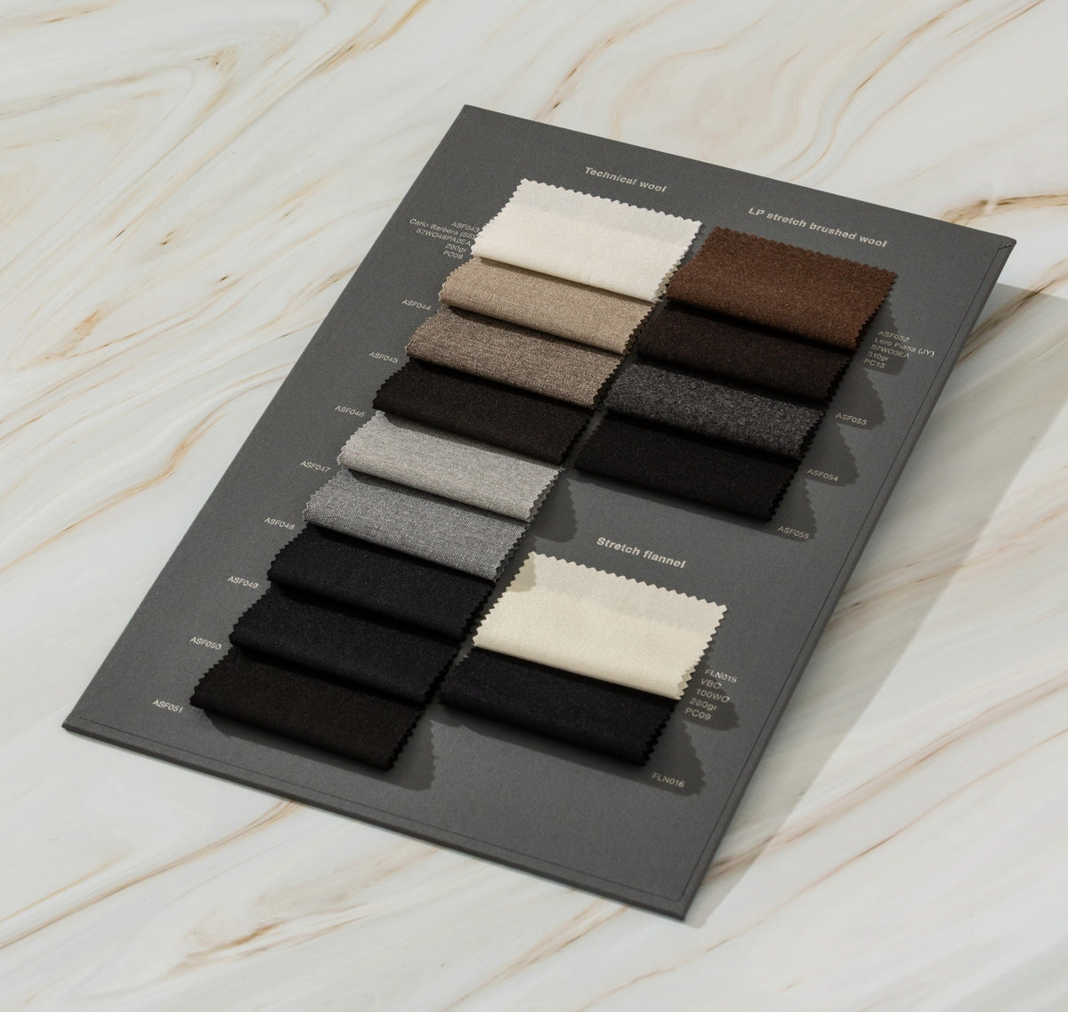 Cream, taupe, grey, brown and black fabric swatches arranged on a dark sample card