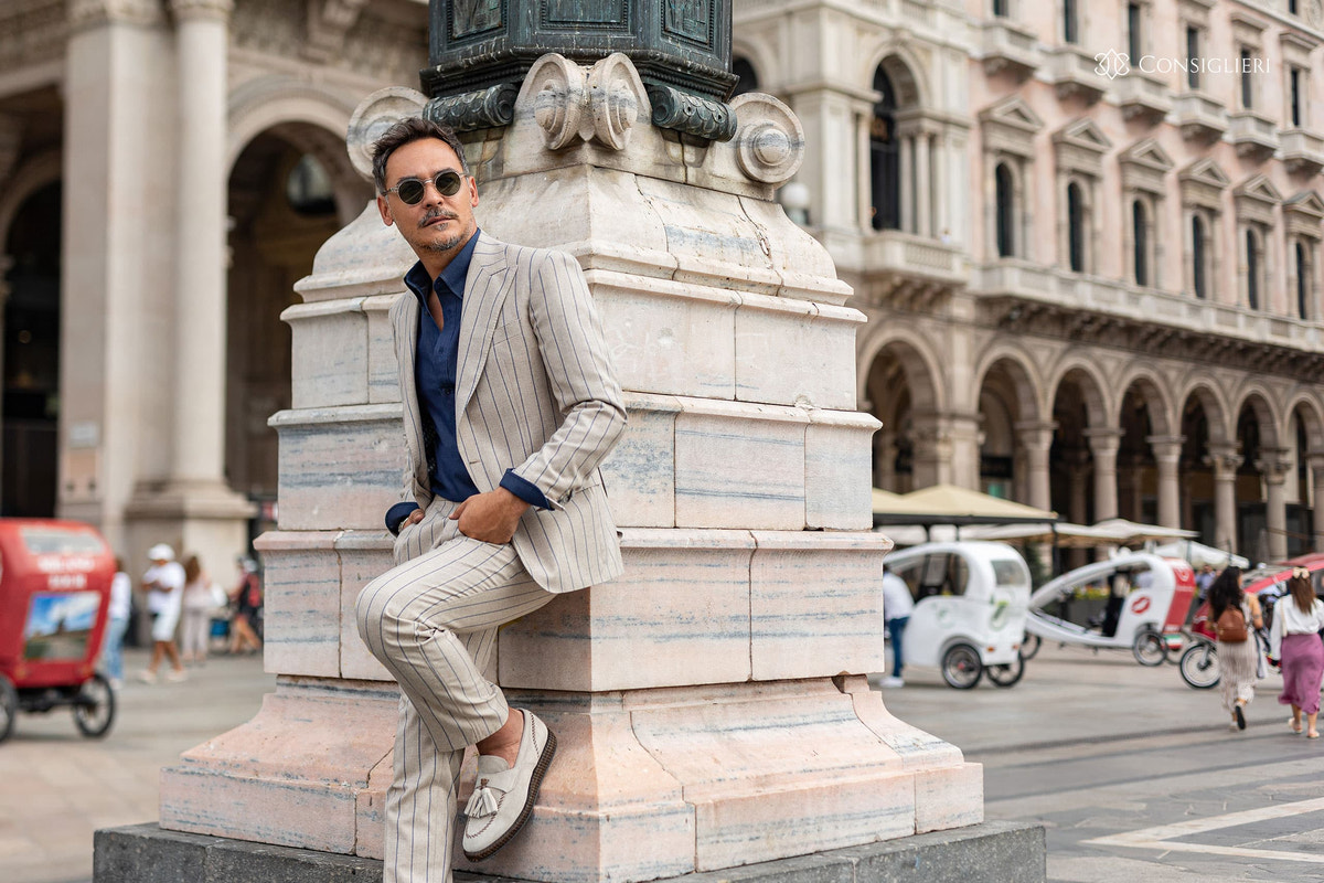 Beige striped Consiglieri suit with a navy shirt in an urban setting