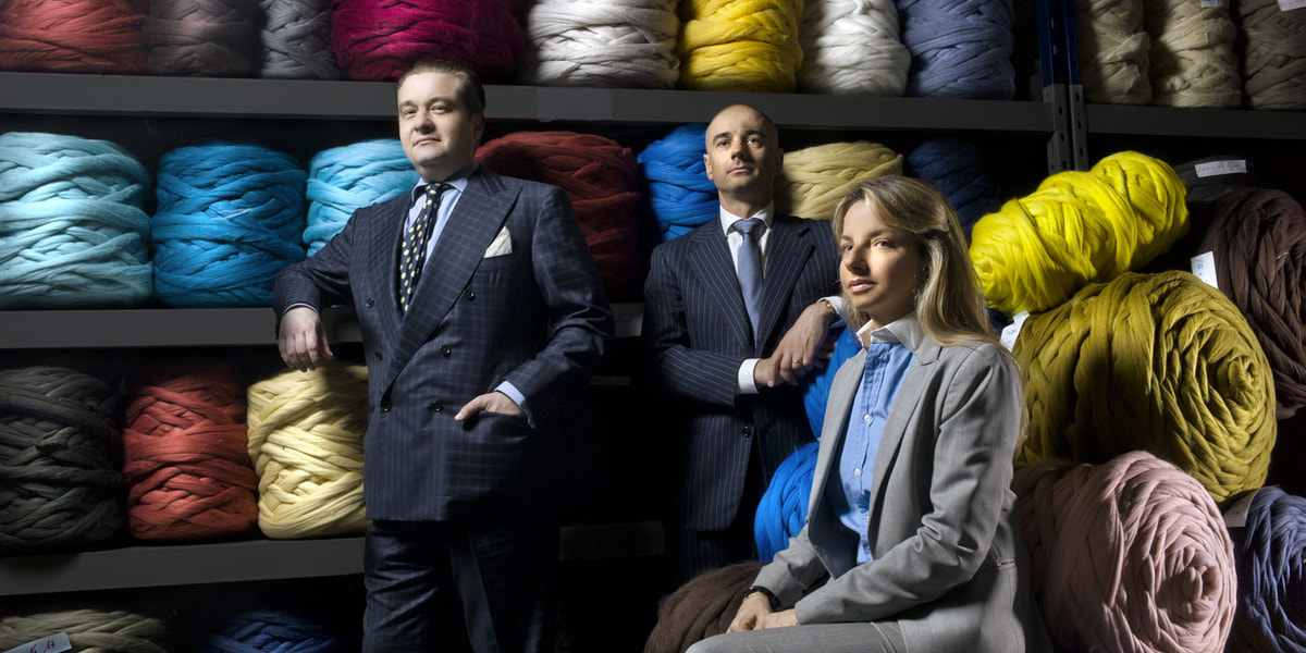 Three men in elegant attire beside a selection of coloured yarns