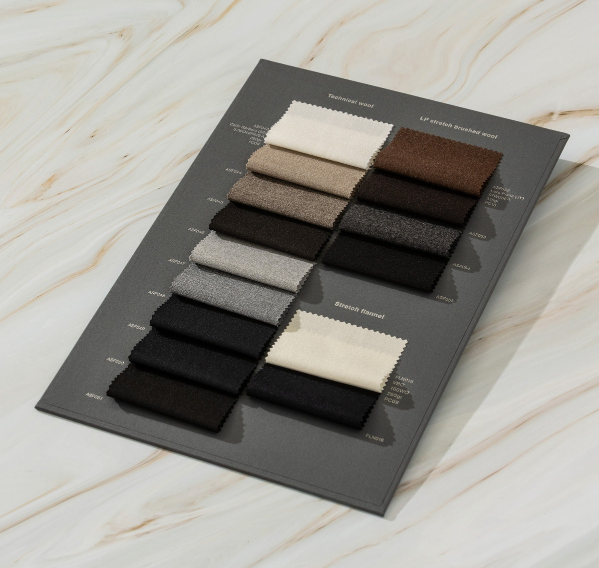 Cream, taupe, grey, brown and black fabric swatches arranged on a dark sample card