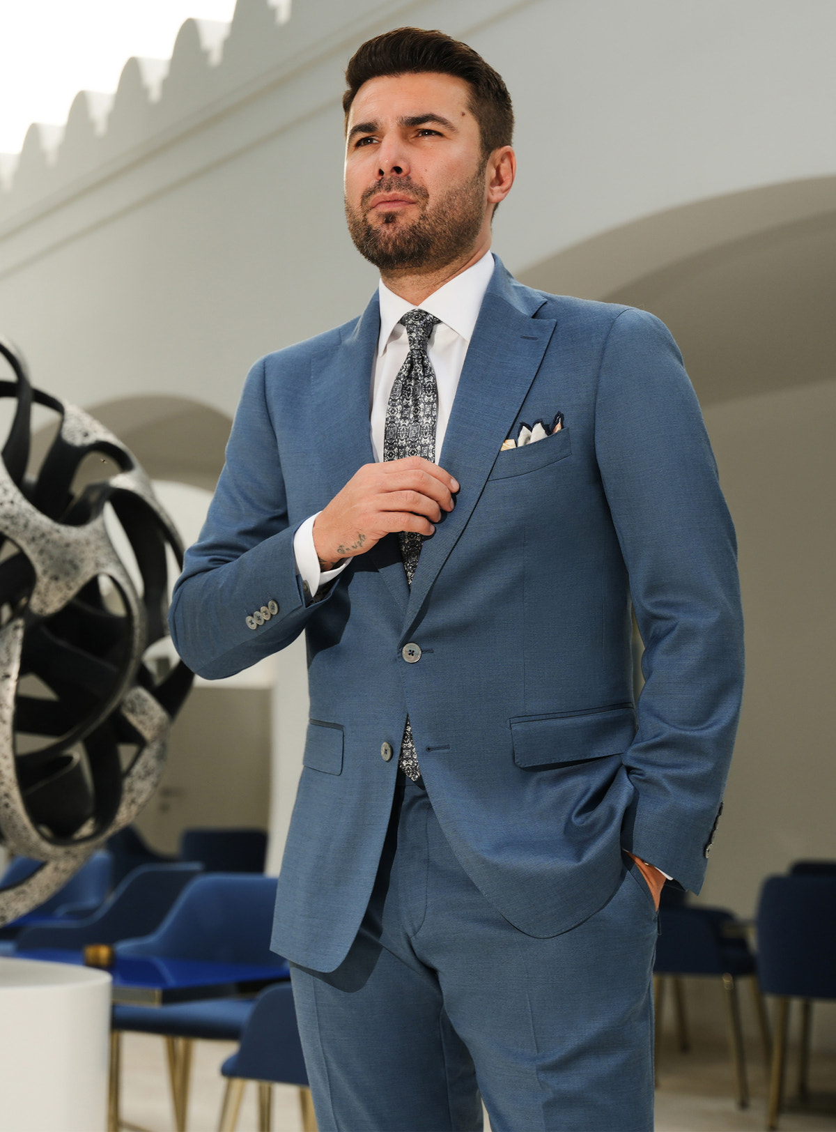 Muted blue Consiglieri suit with notch lapels, a white shirt and patterned tie