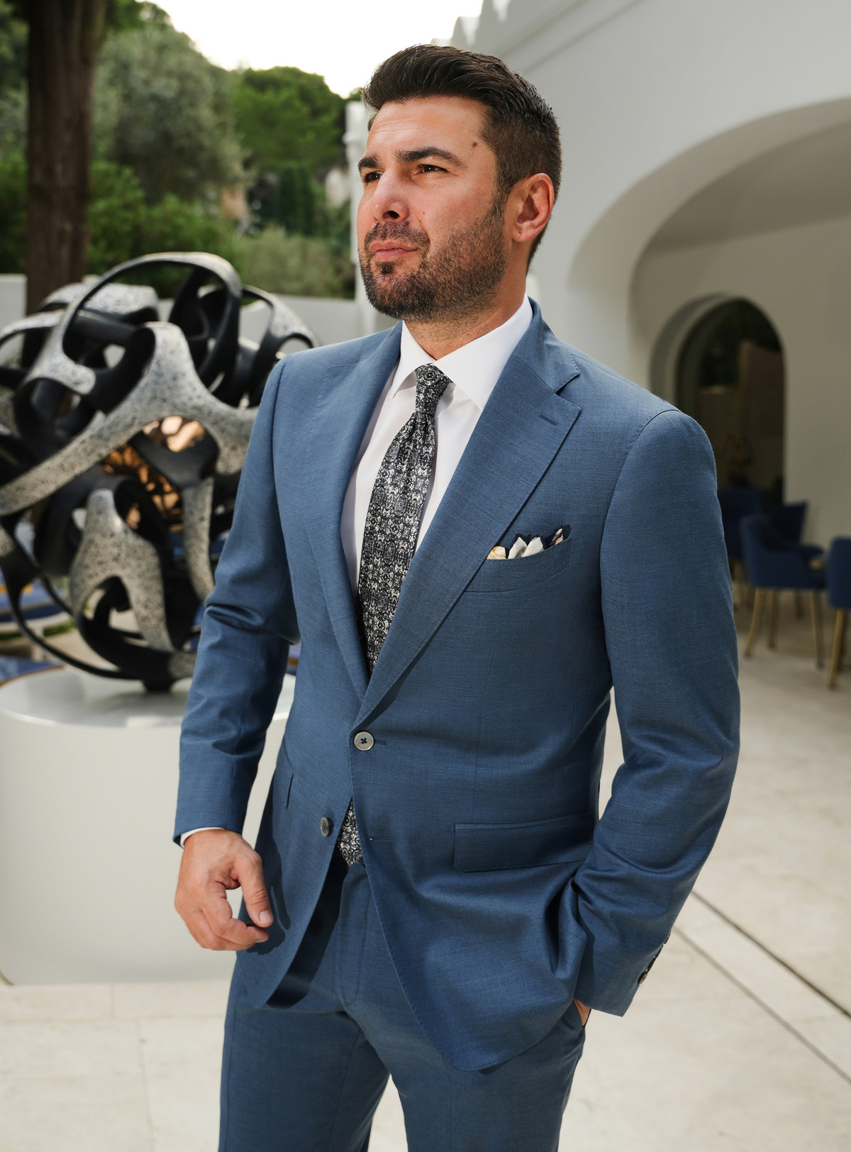 Muted blue Consiglieri suit with notch lapels, a white shirt and patterned tie