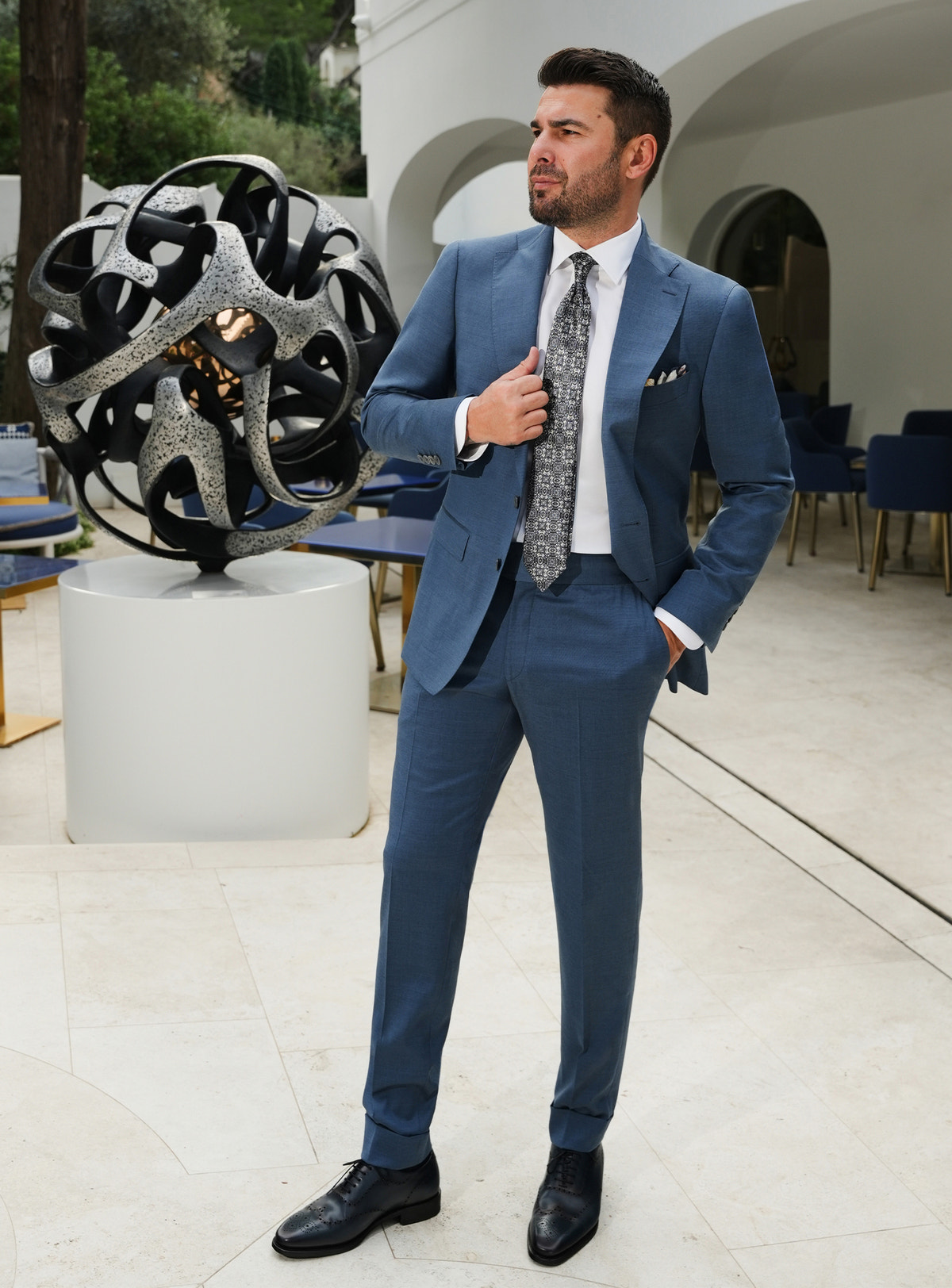 Muted blue Consiglieri suit with notch lapels, a white shirt and patterned tie