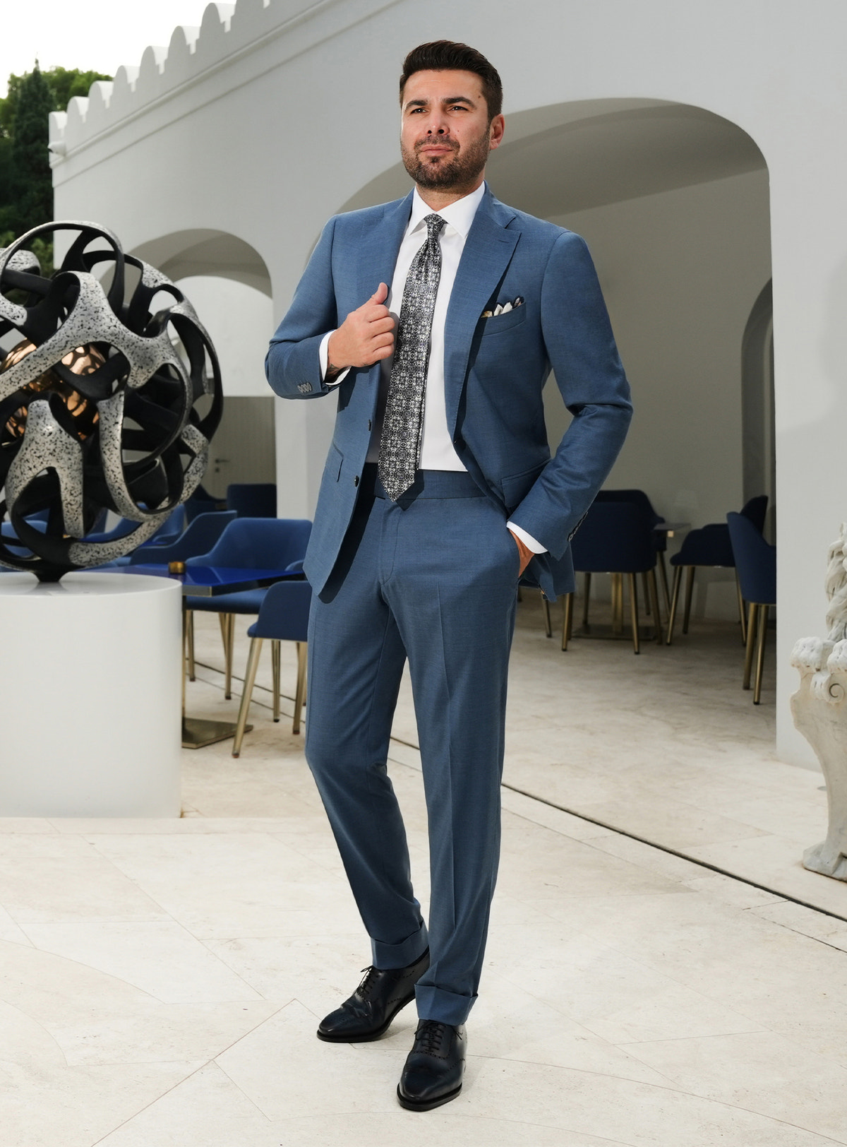 Muted blue Consiglieri suit with notch lapels, a white shirt and patterned tie