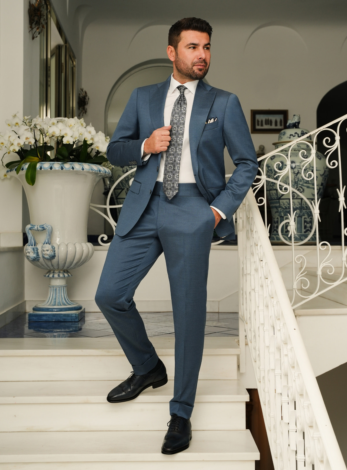 Muted blue Consiglieri suit with notch lapels, a white shirt and patterned tie