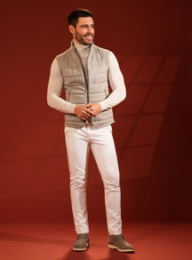 Grey-beige quilted Consiglieri vest over an ivory turtleneck, with white trousers