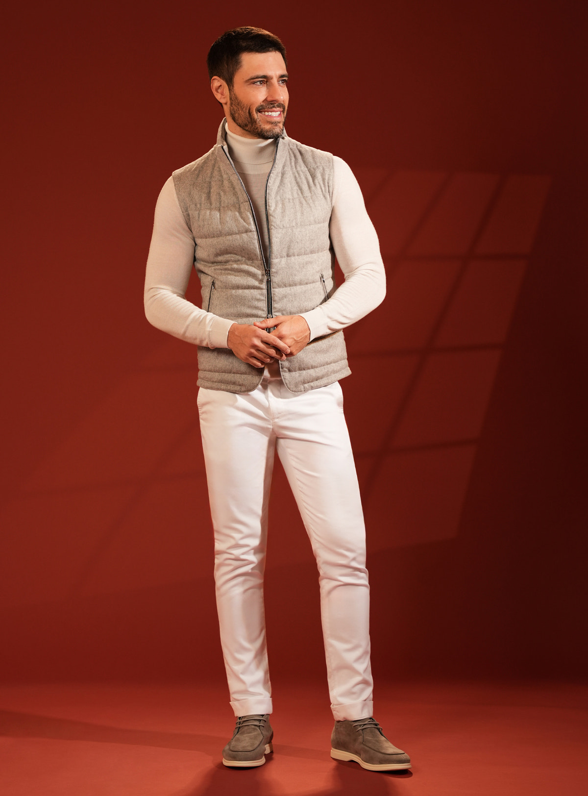 Grey-beige quilted Consiglieri vest over an ivory turtleneck, with white trousers