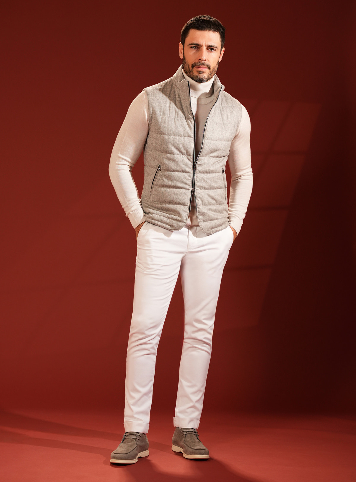Grey-beige quilted Consiglieri vest over an ivory turtleneck, with white trousers