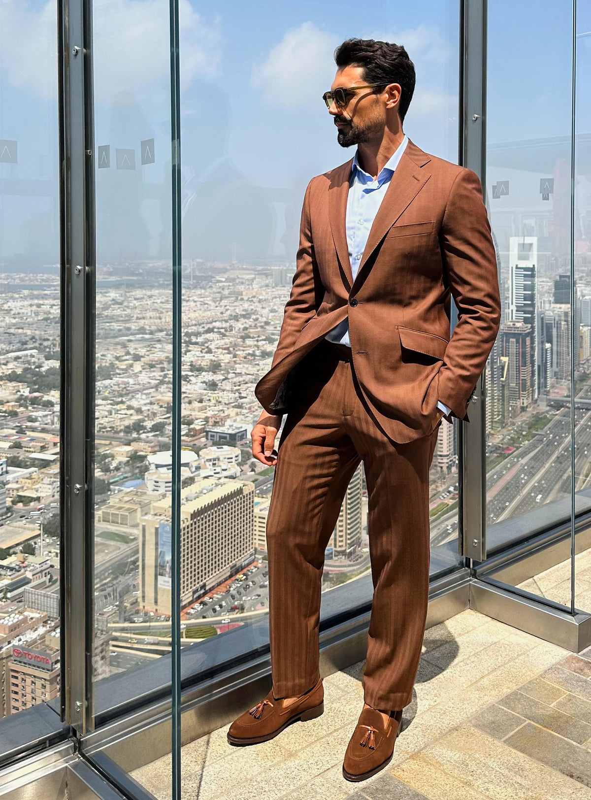 Terracotta Consiglieri suit in a complete look beside panoramic windows