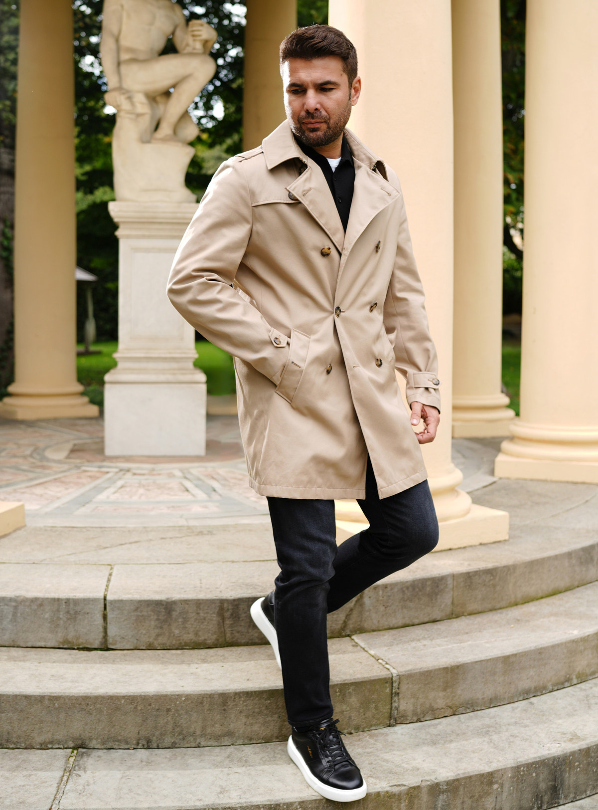 Black Consiglieri jeans worn with a beige double-breasted trench coat