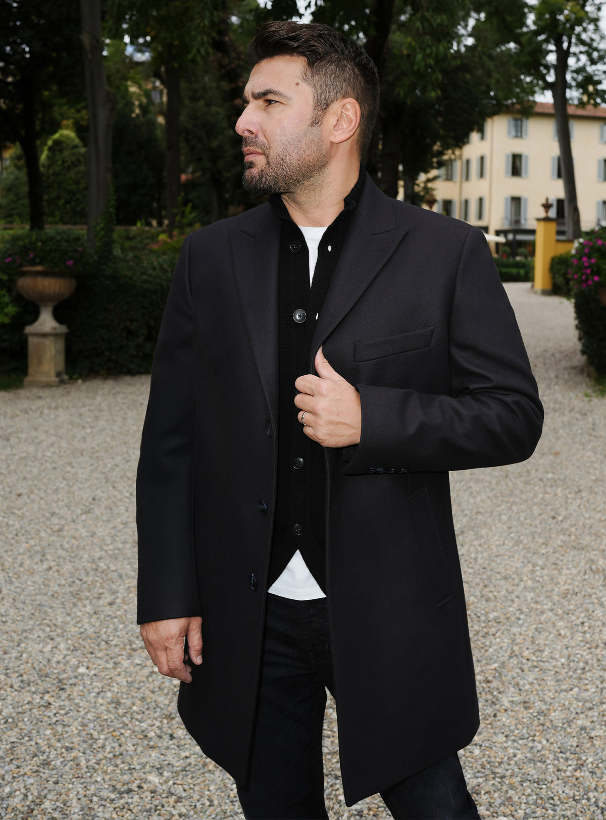 Black Consiglieri overcoat with notch lapels, styled with a black cardigan and trousers