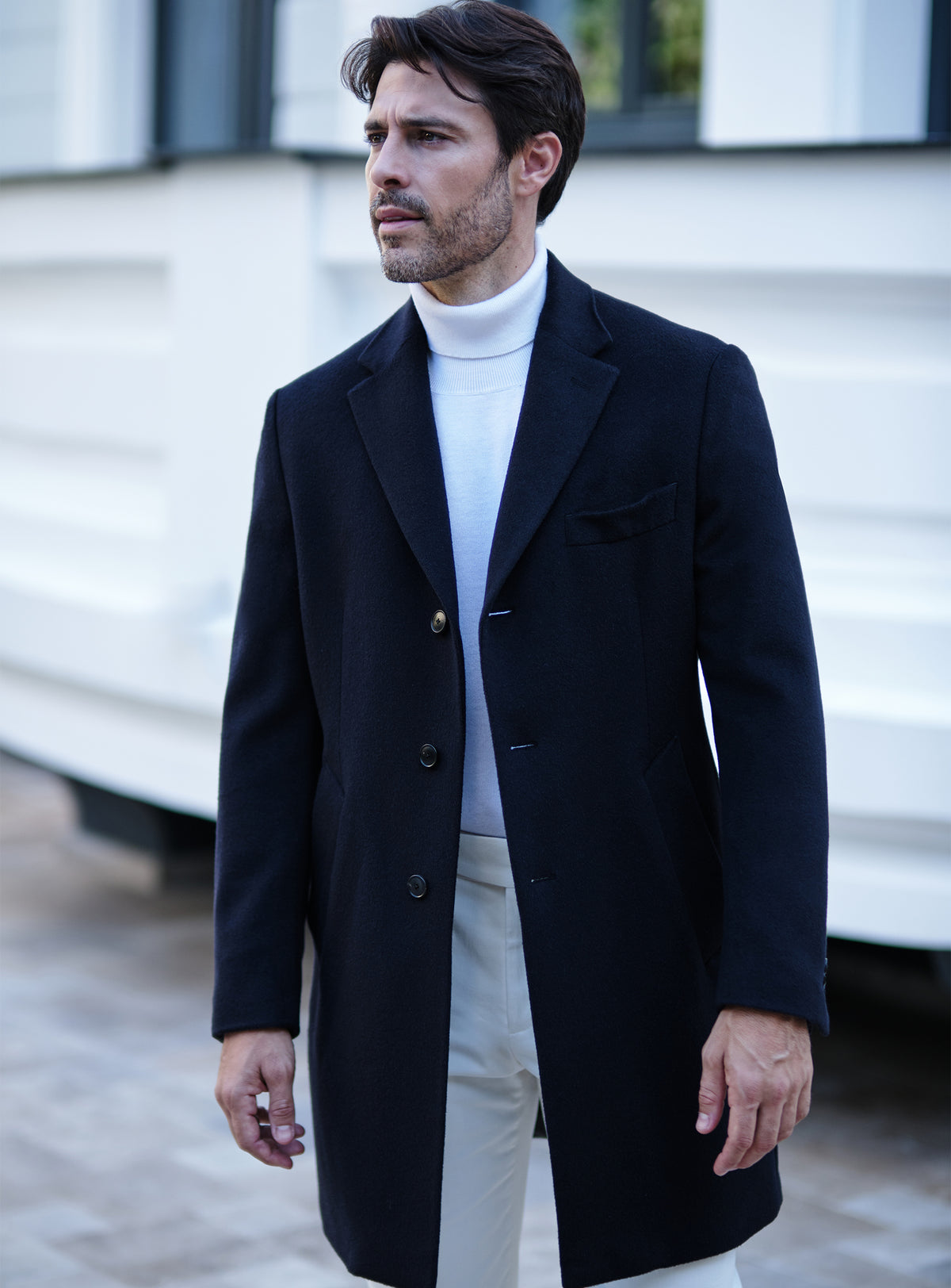 Navy Consiglieri overcoat with notch lapels, a white turtleneck and white trousers