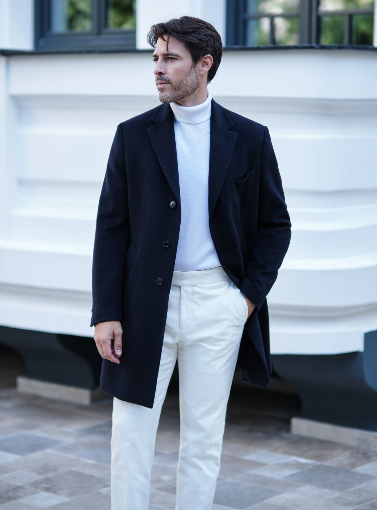 Navy Consiglieri overcoat with notch lapels, a white turtleneck and white trousers