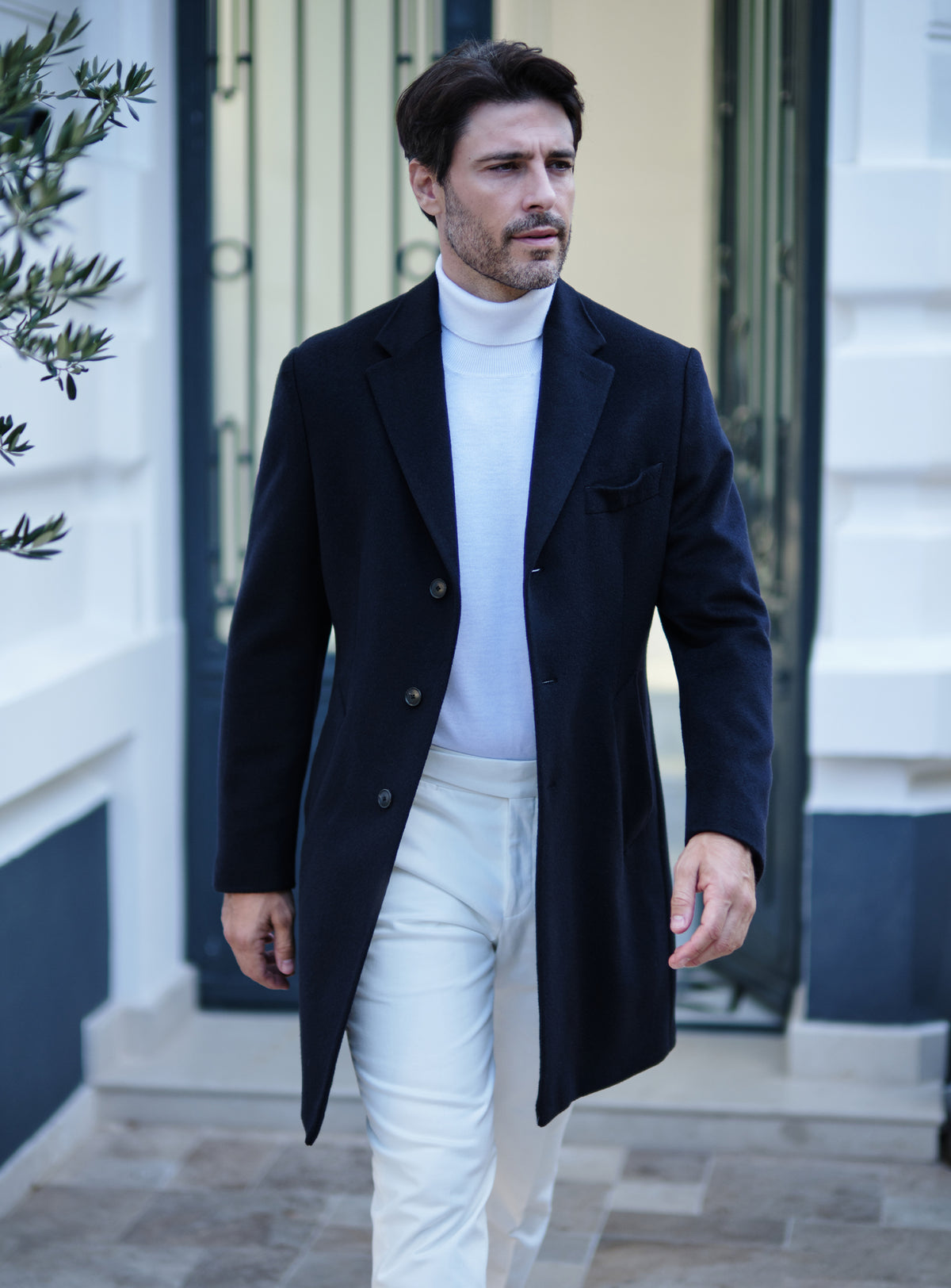 Navy Consiglieri overcoat with notch lapels, a white turtleneck and white trousers