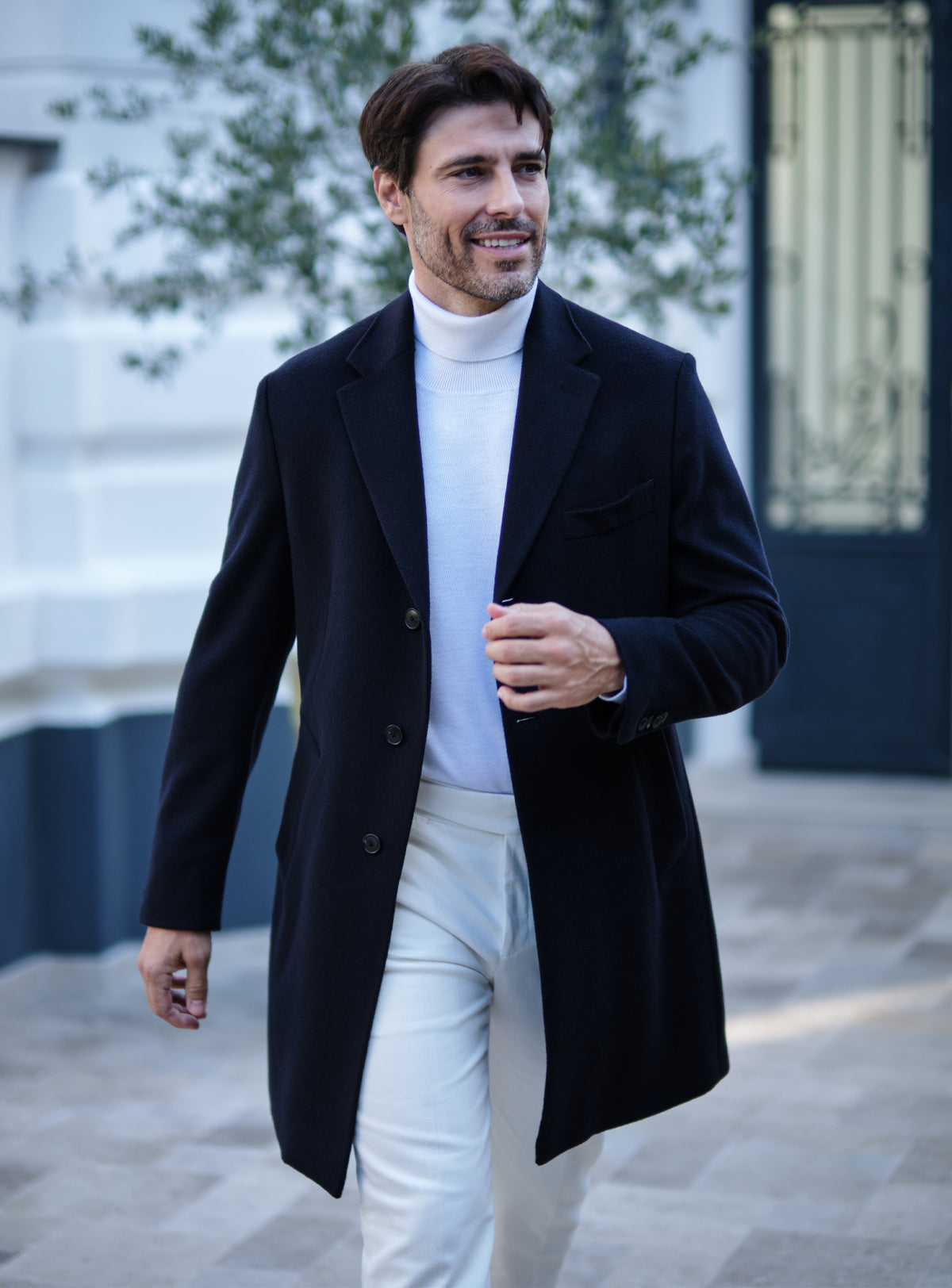 Navy Consiglieri overcoat with notch lapels, a white turtleneck and white trousers