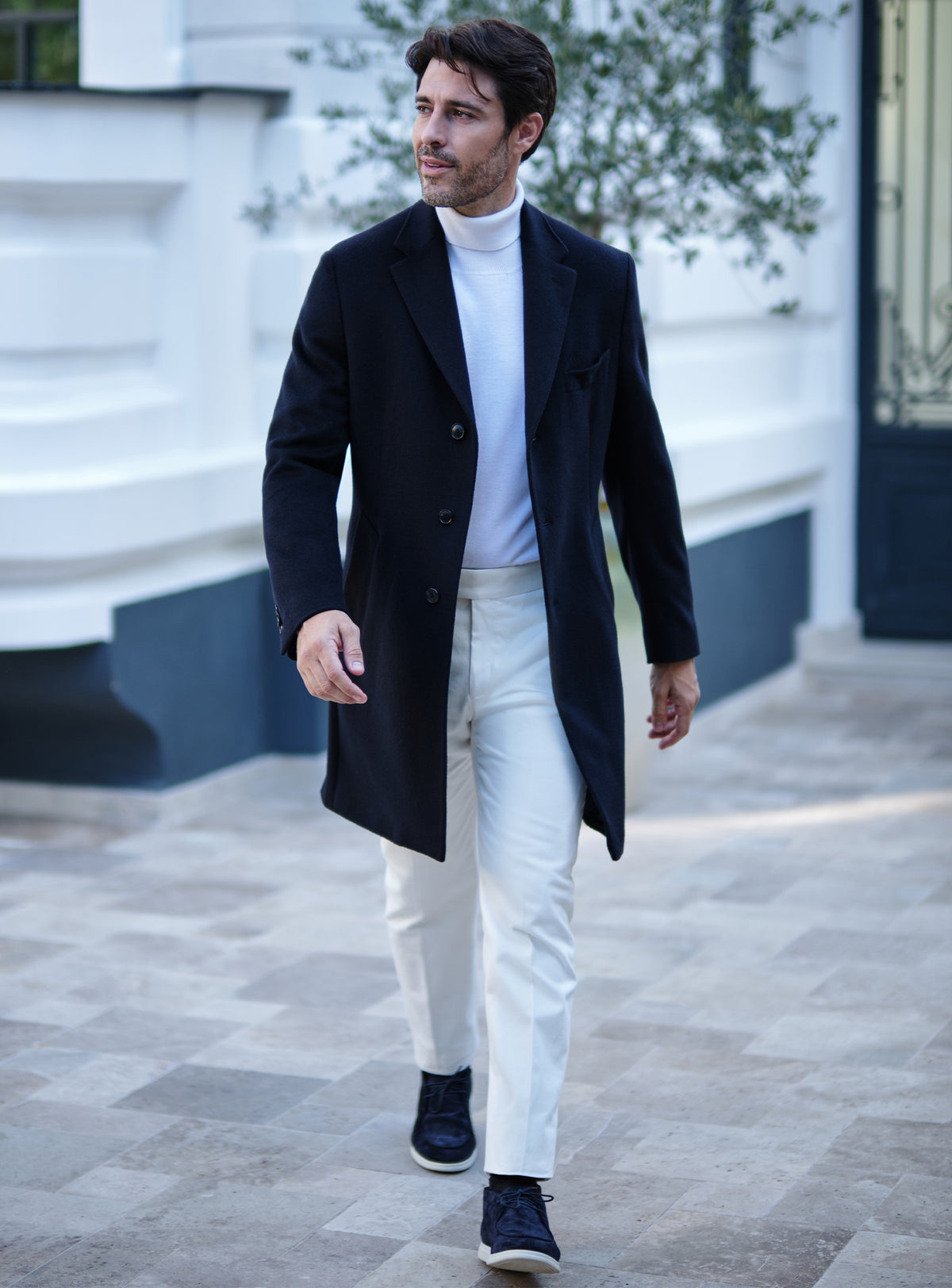 Navy Consiglieri overcoat with notch lapels, a white turtleneck and white trousers