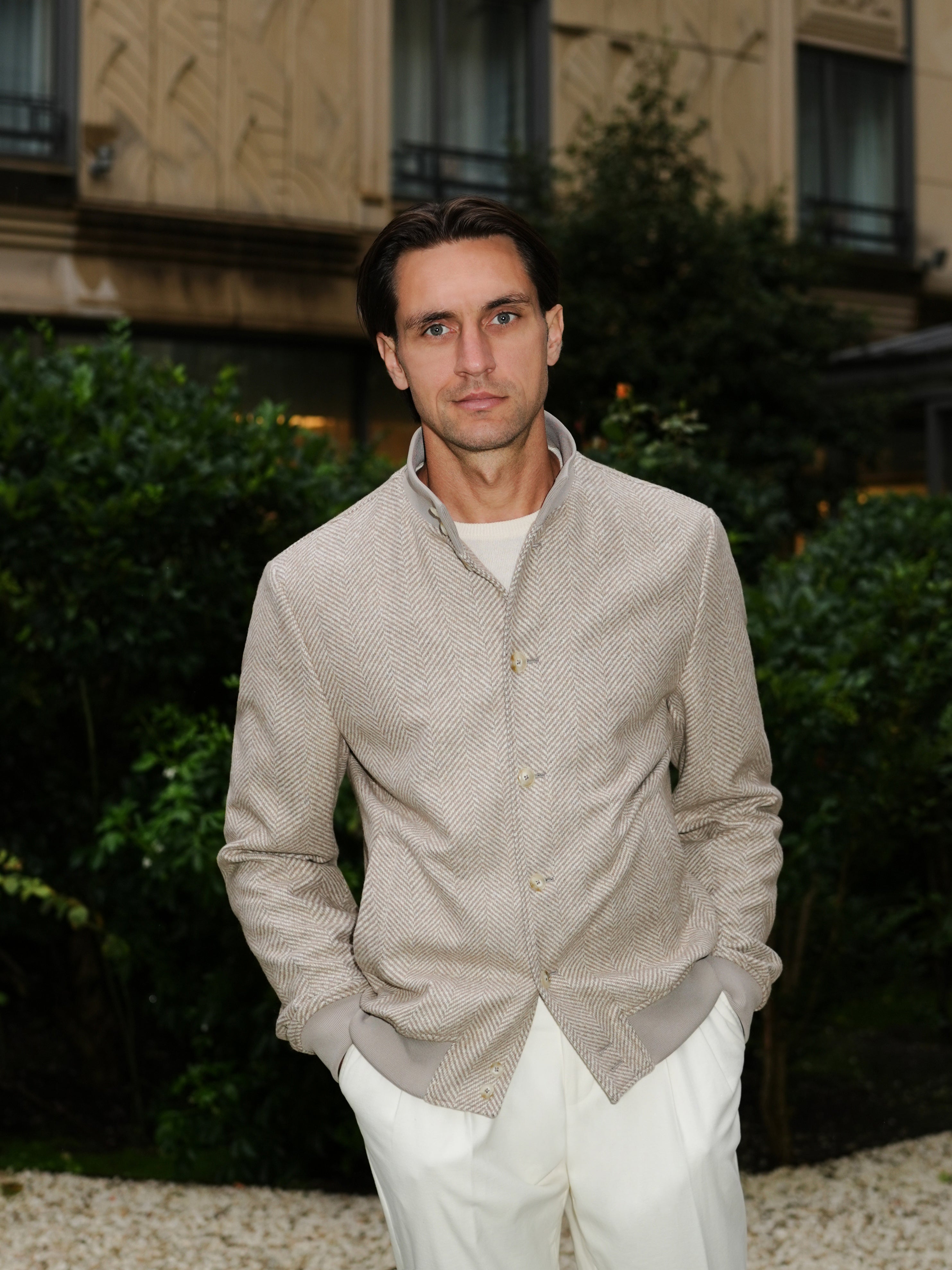 Portrait with a grey-beige textured blouson and white trousers in a garden setting