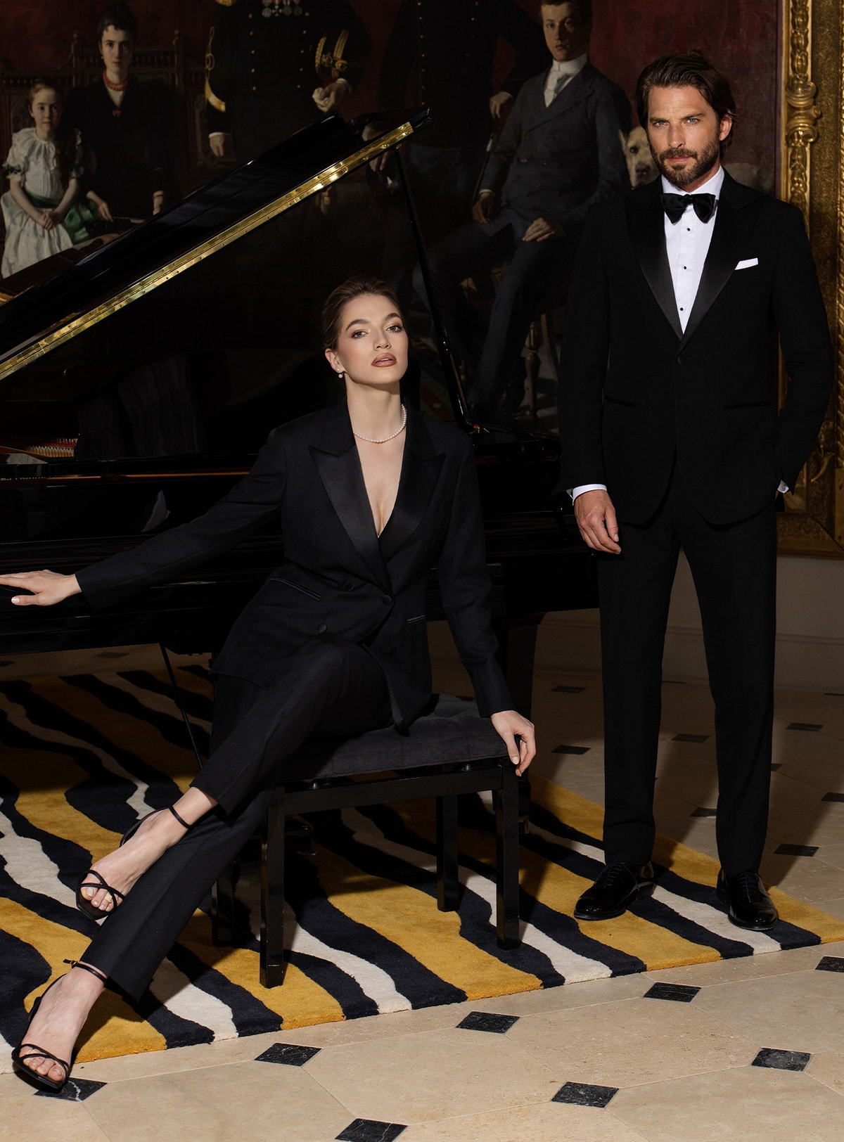 Black Consiglieri women's and men's tuxedos beside a piano