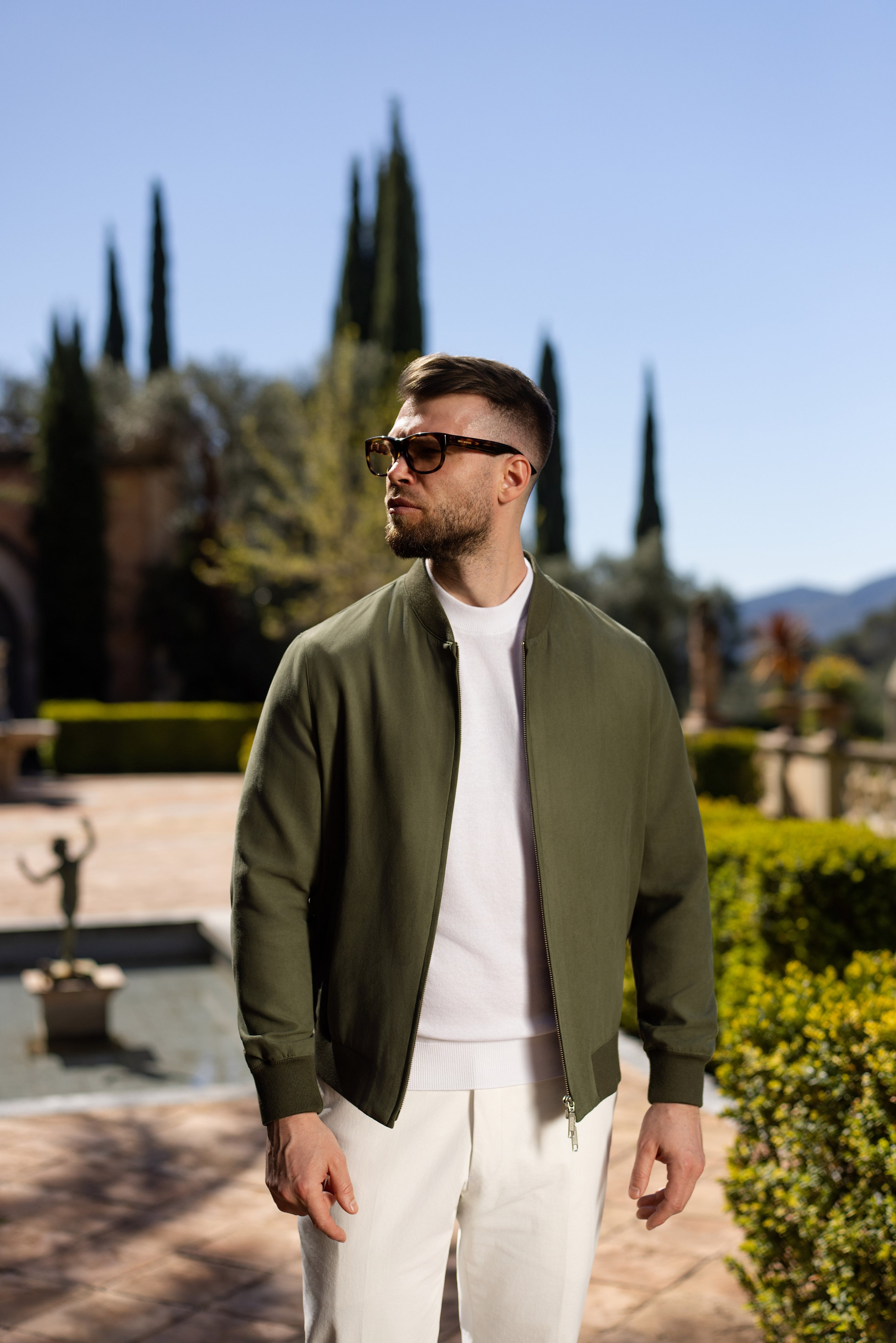 Olive Bomber jacket worn in a light-toned outfit, in a garden setting