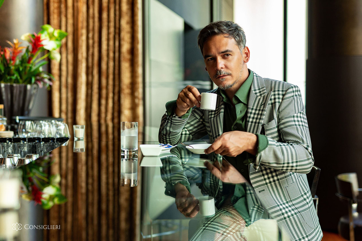 Green striped Consiglieri suit with a dark shirt in an elegant interior