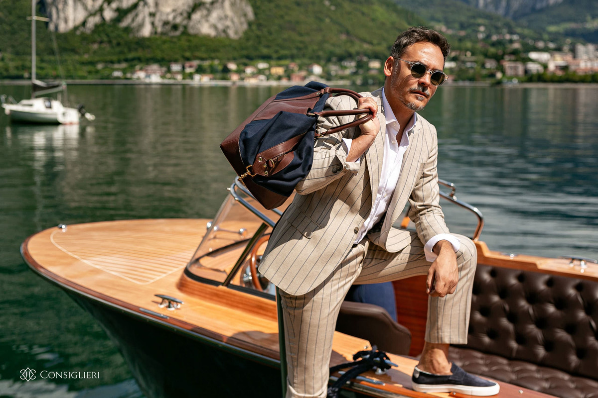 Beige Consiglieri suit with a shoulder bag beside a wooden boat