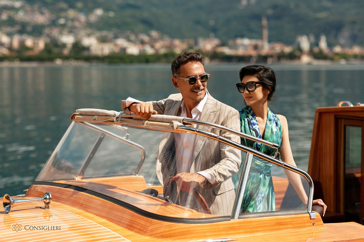 Beige suit and a green-blue printed dress in a couple's scene aboard a boat