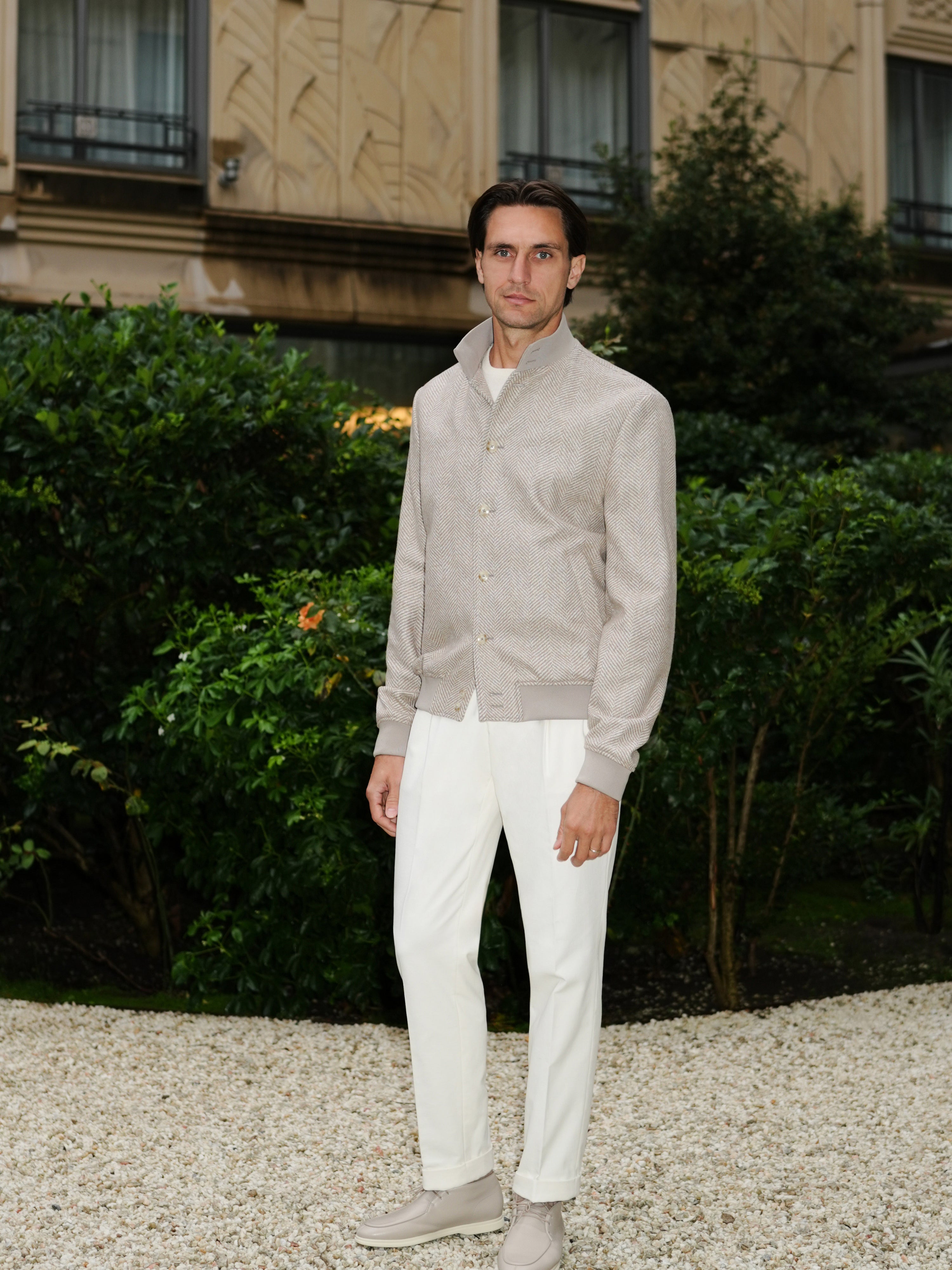Complete outfit with a grey-beige textured blouson, photographed in a garden