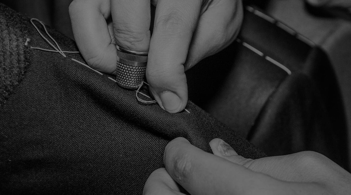 Hands finishing a seam in a black-and-white photograph of Consiglieri tailoring