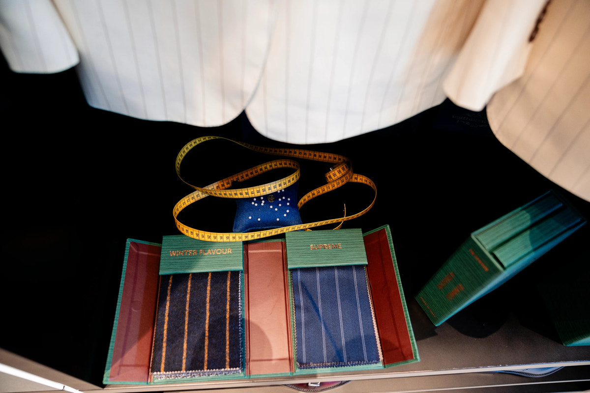 Striped fabric swatches and a tailor’s tape measure beside light-toned garments.