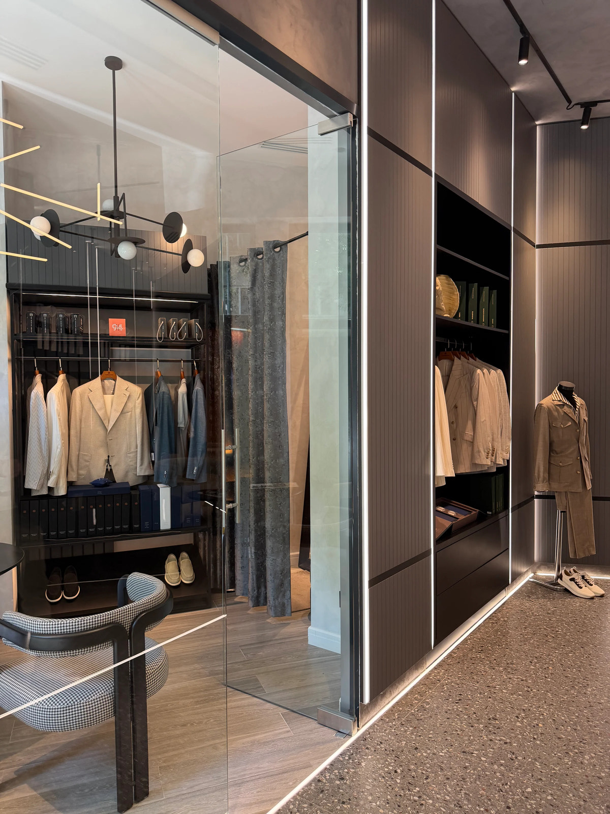 Jackets displayed beyond a glass partition, beside a beige outfit.