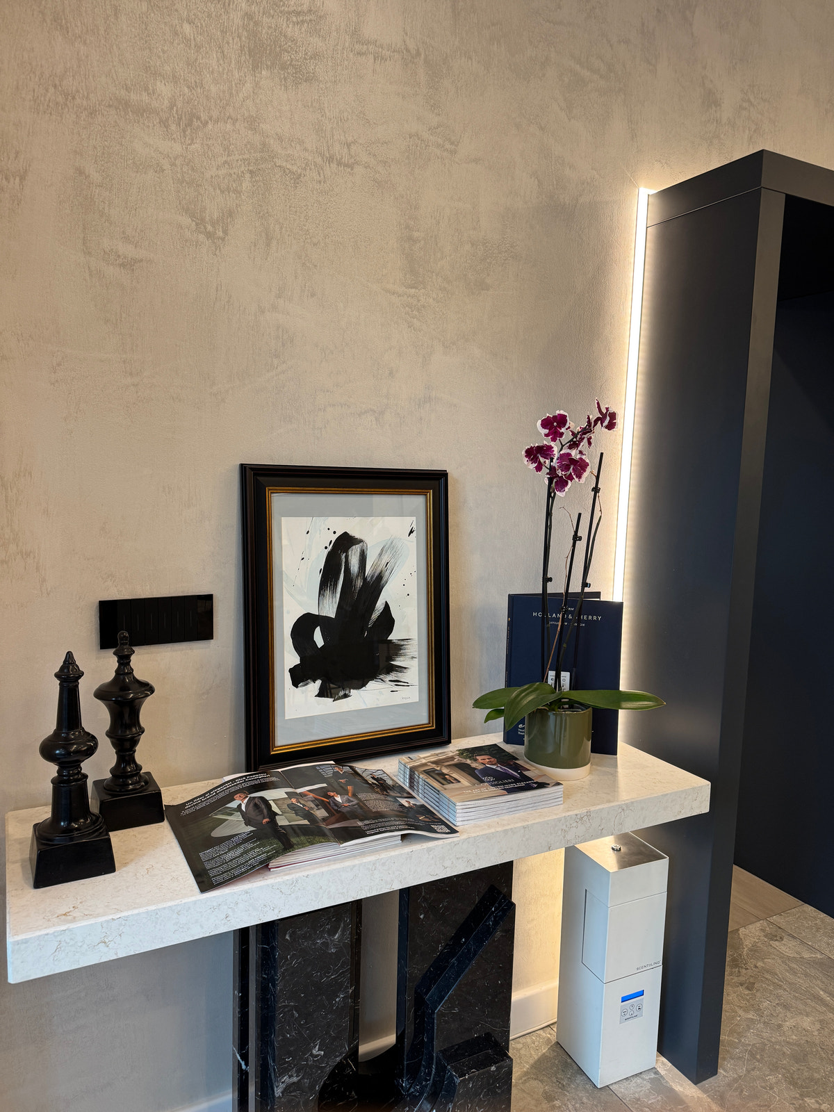 Books and artwork beside an orchid on a light-coloured console.