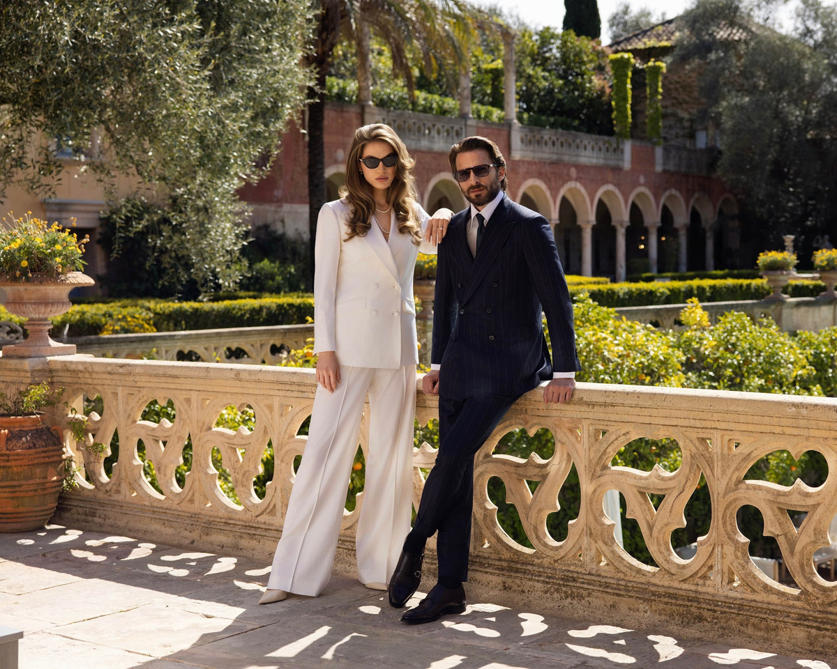 A couple in an ivory women's suit and a dark men's suit beside a balustrade