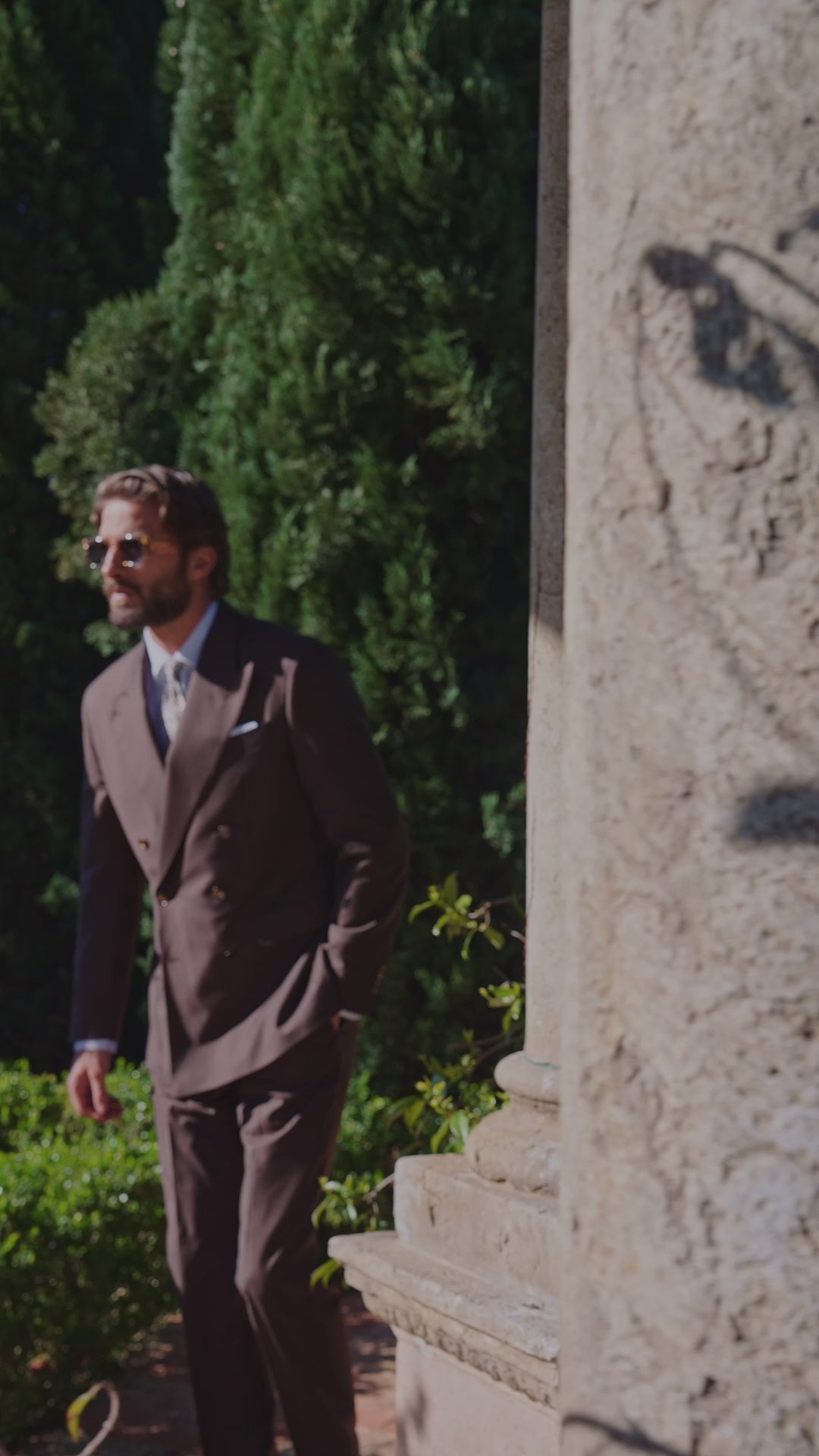 Men’s brown double-breasted suit beside columns and greenery