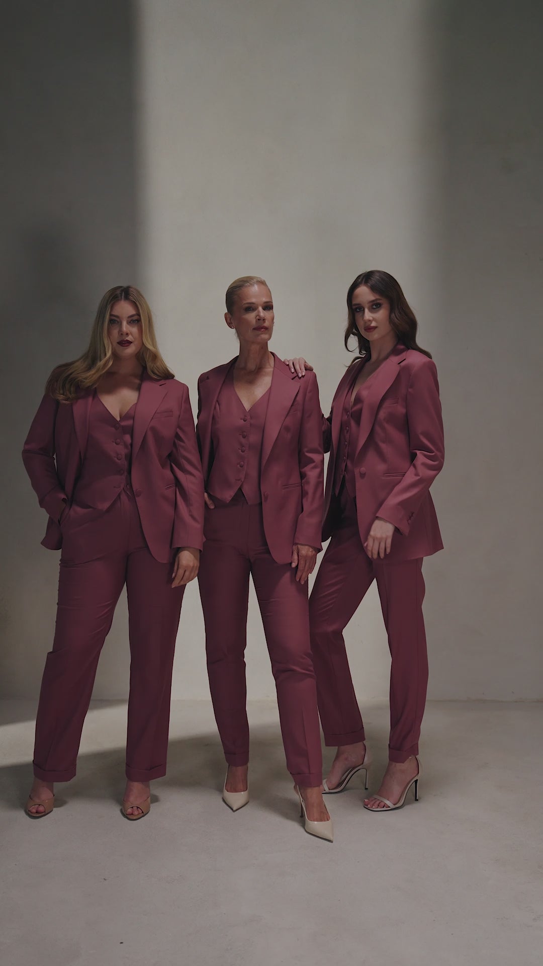 Three women in burgundy Consiglieri The Vendôme Suit ensembles with jackets and waistcoats