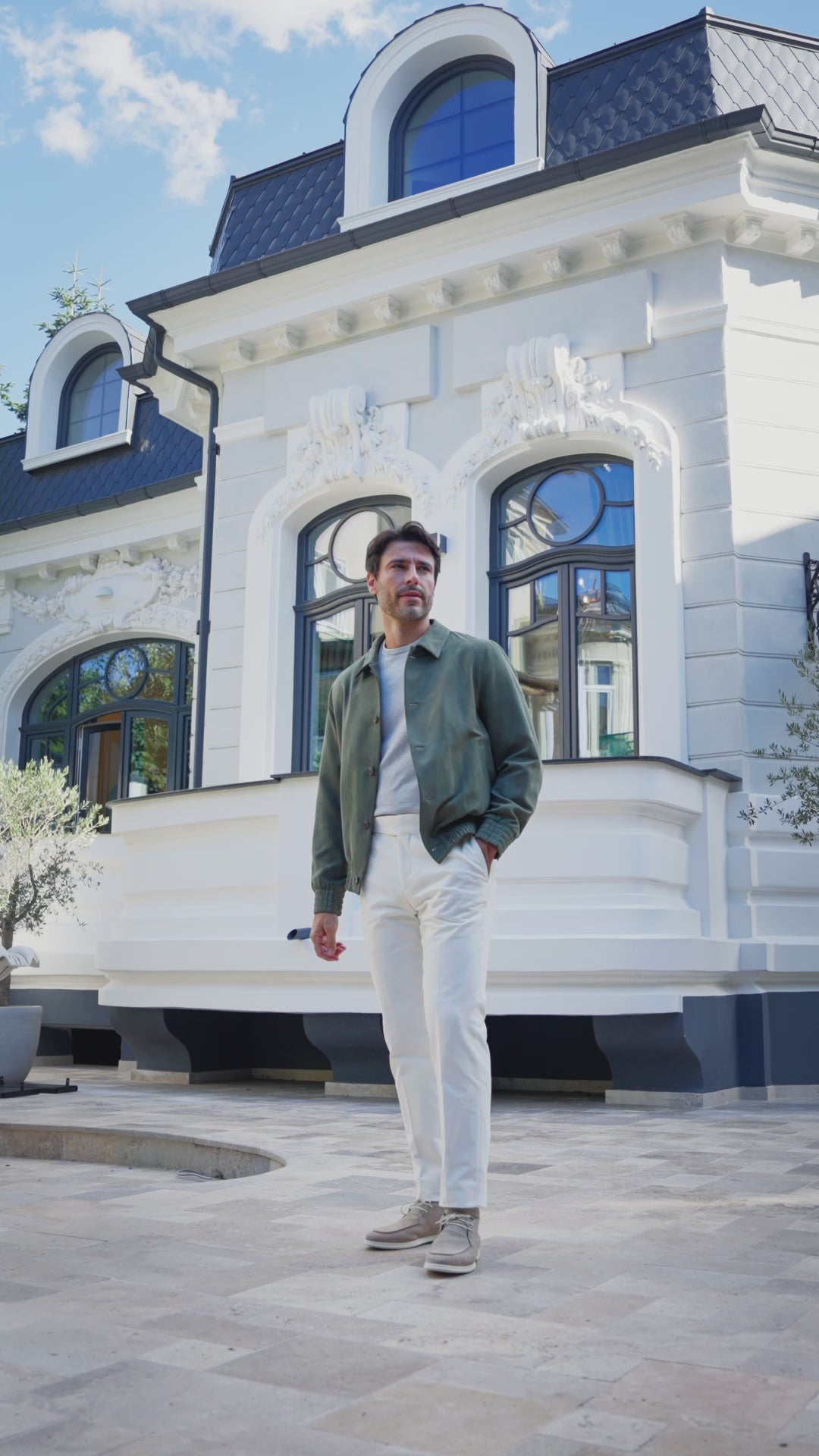 Green jacket and white trousers outside a building with arched windows