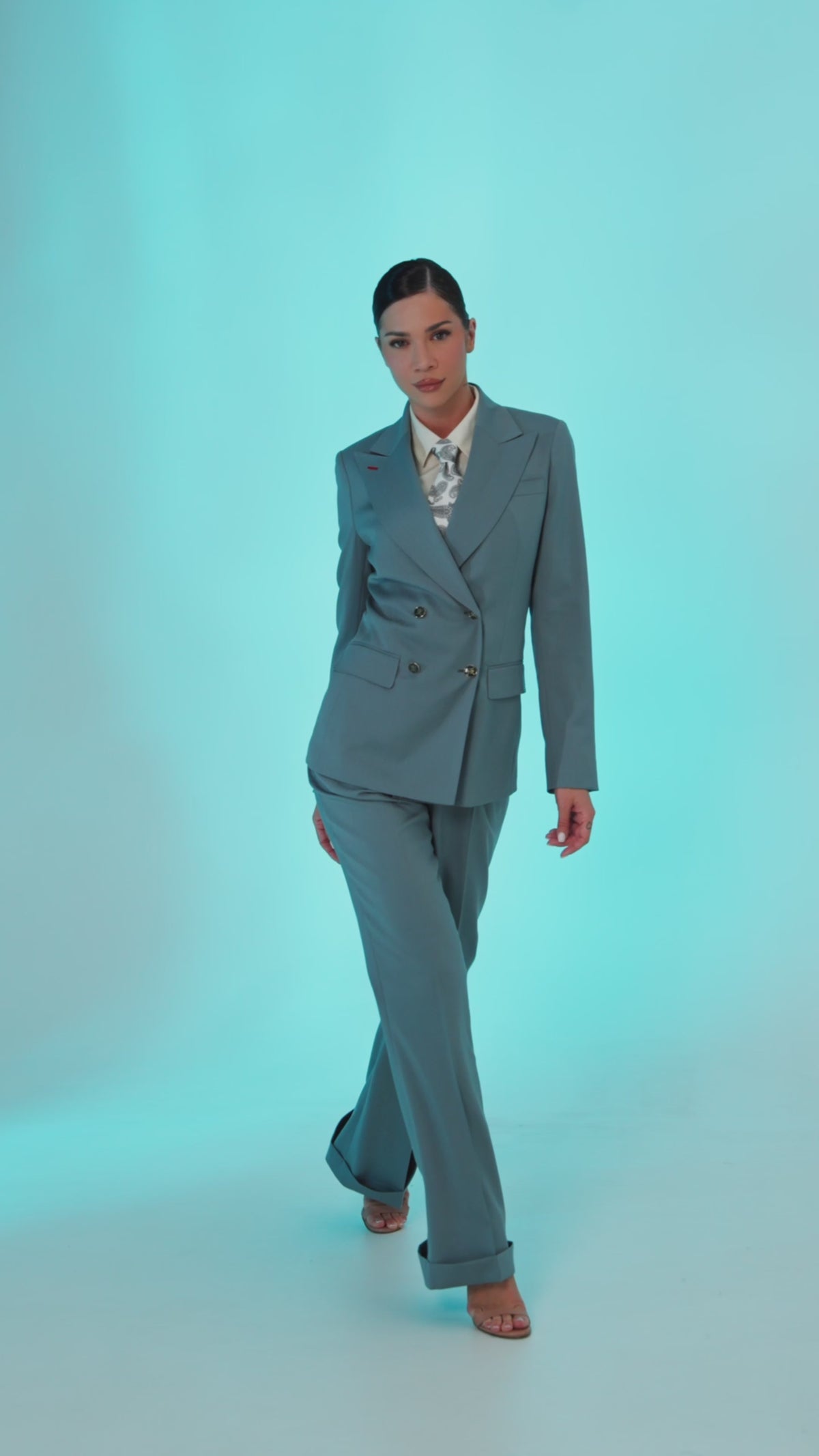 Women’s grey double-breasted suit with a patterned shirt against a turquoise background