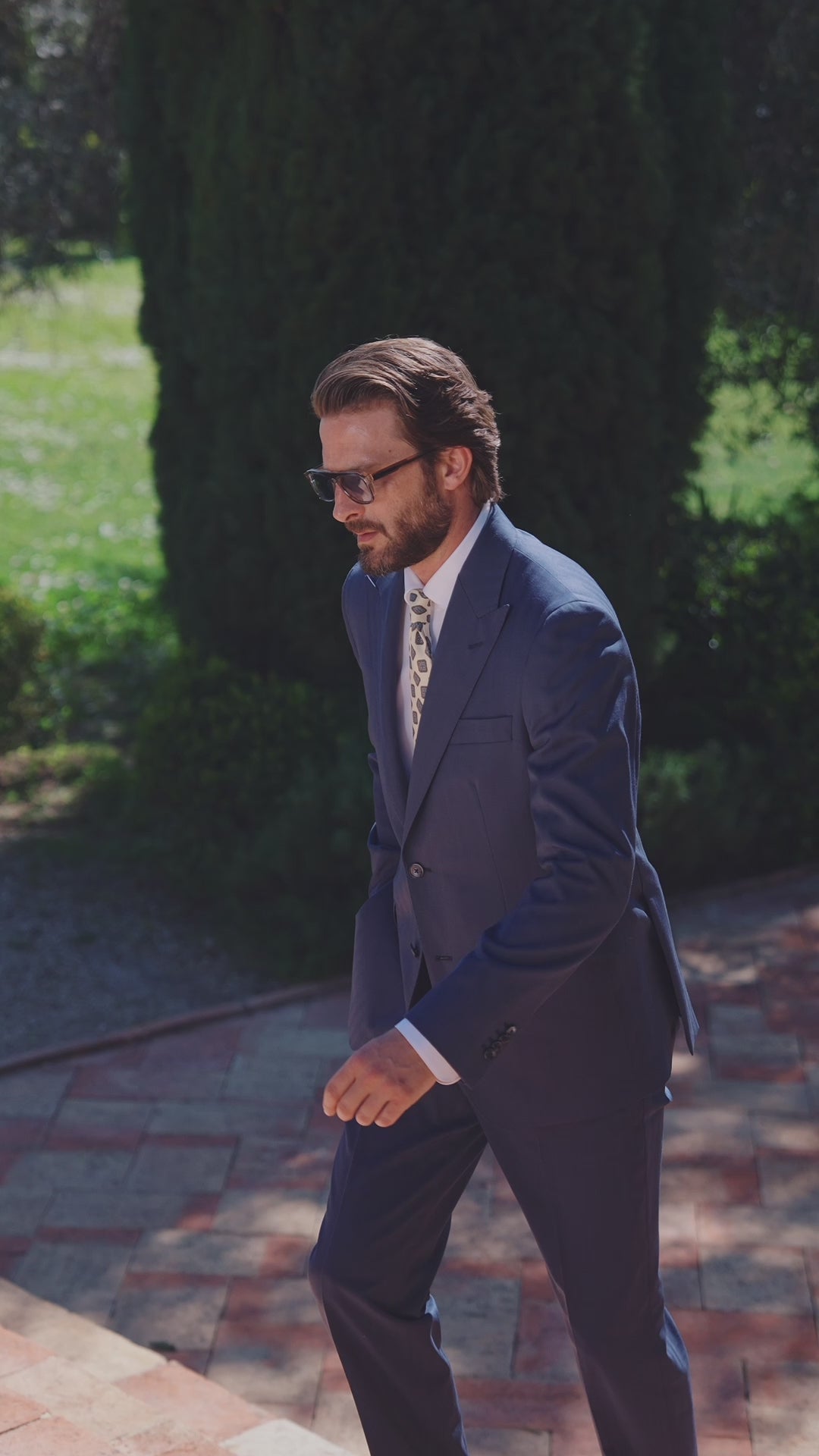 Men’s navy suit with a white shirt and tie on a shaded path