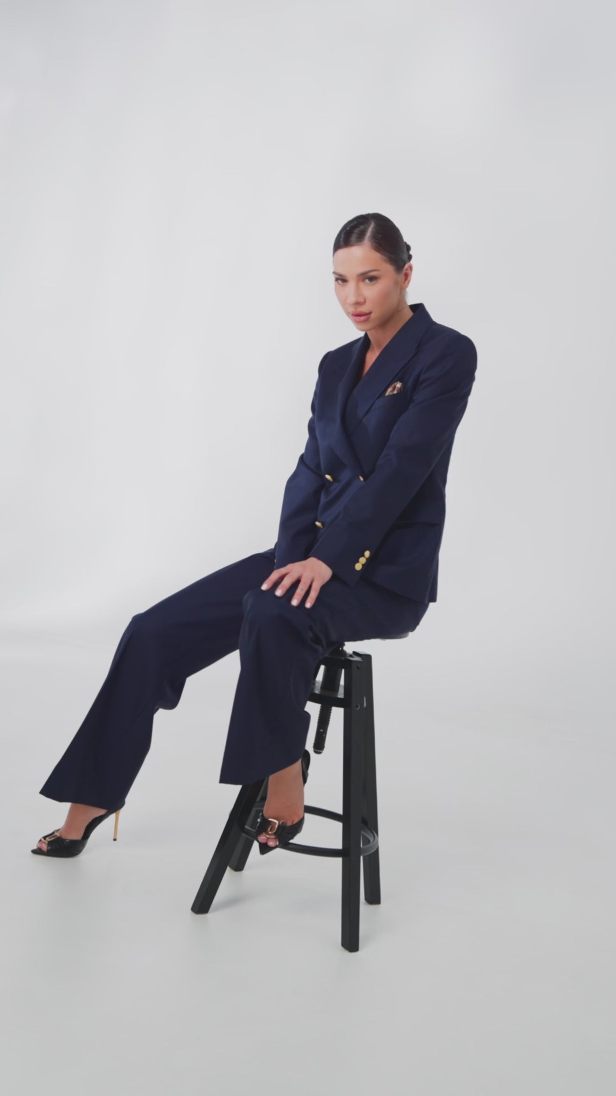 Woman in a navy suit and black heels seated on a high stool