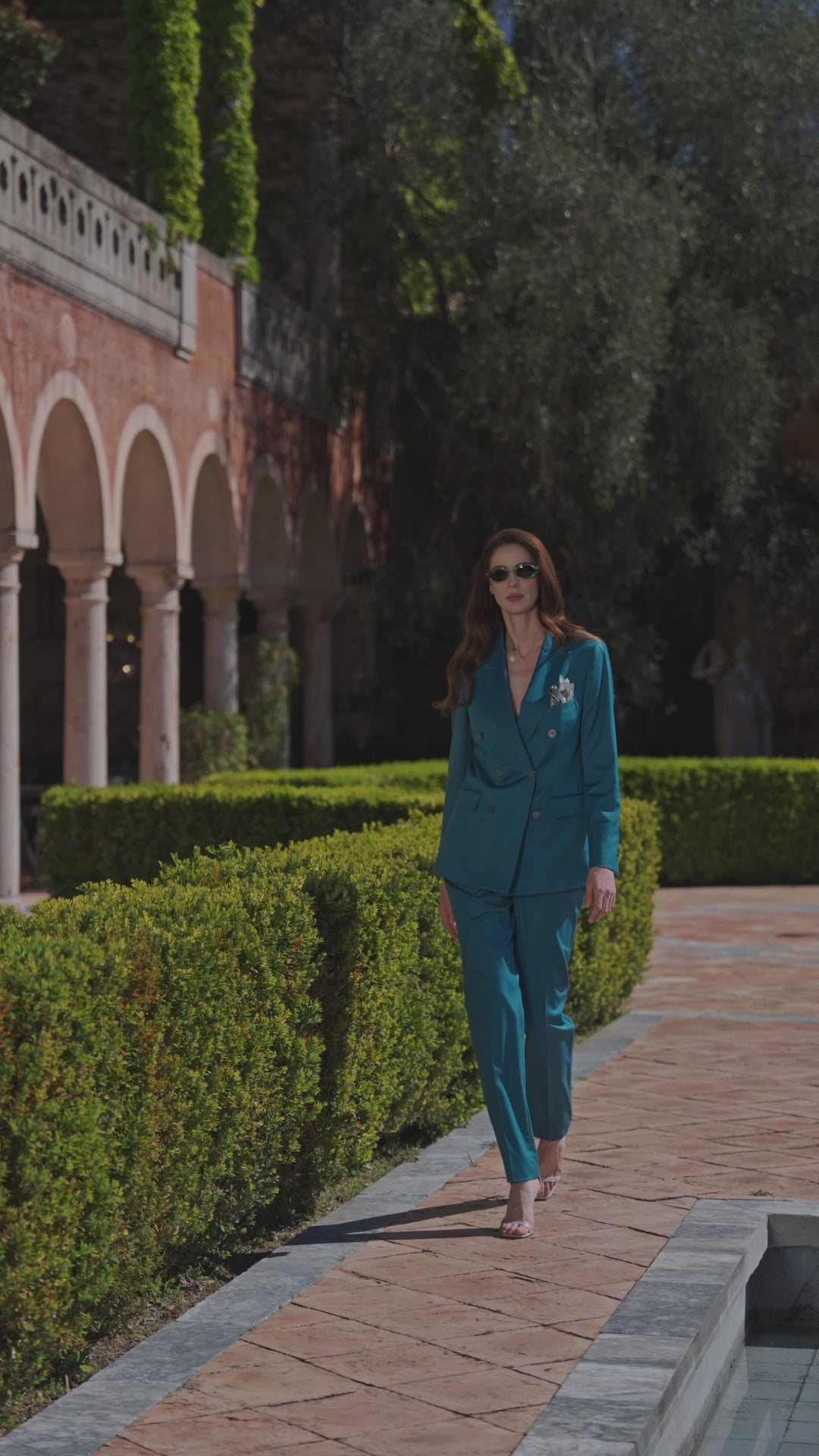 Teal Consiglieri Amalfi women's suit on a path lined with hedges