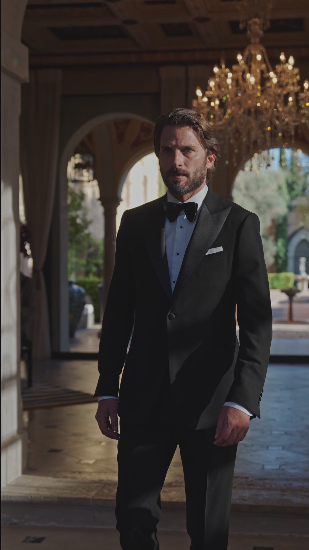 Black Consiglieri tuxedo with a bow tie in an elegant interior with a chandelier