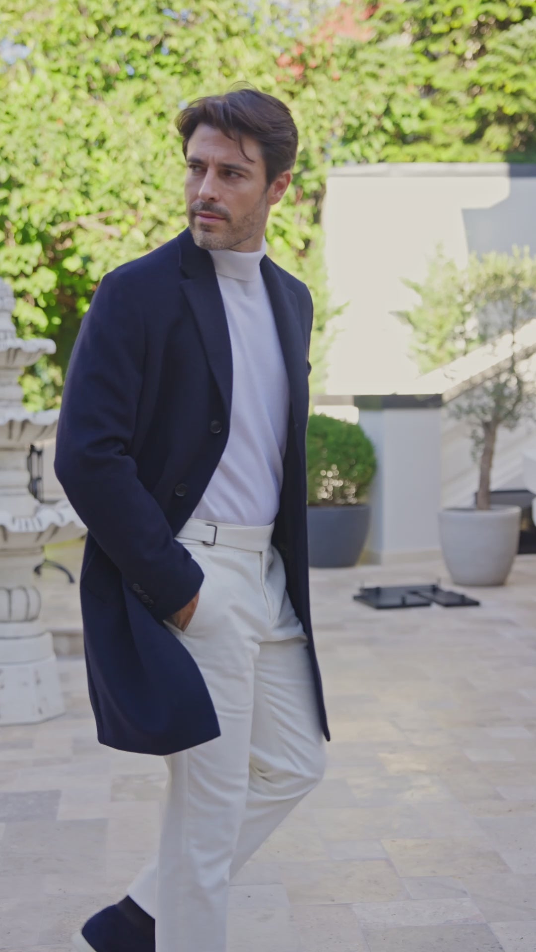 Navy overcoat and white trousers in a sunlit courtyard