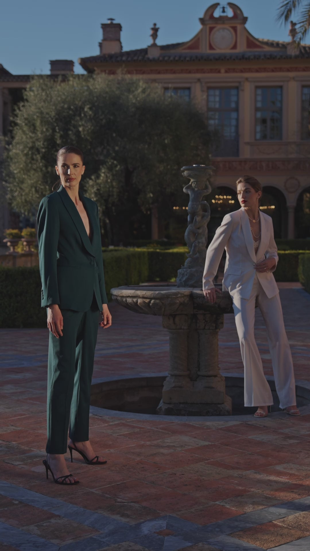 Two women in emerald green and ivory Consiglieri suits beside a fountain
