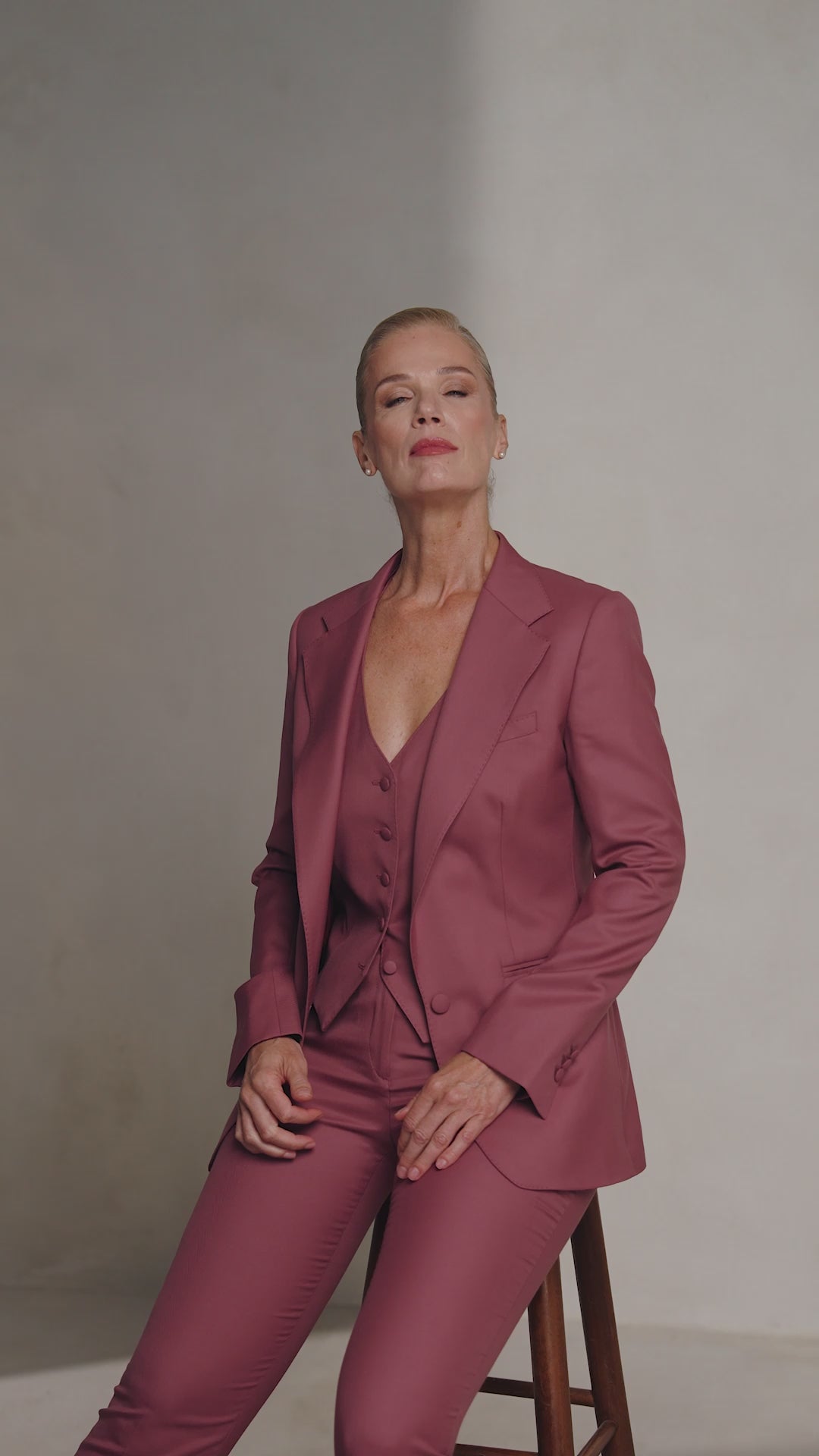 A woman seated on a stool in a burgundy Consiglieri The Vendôme Suit
