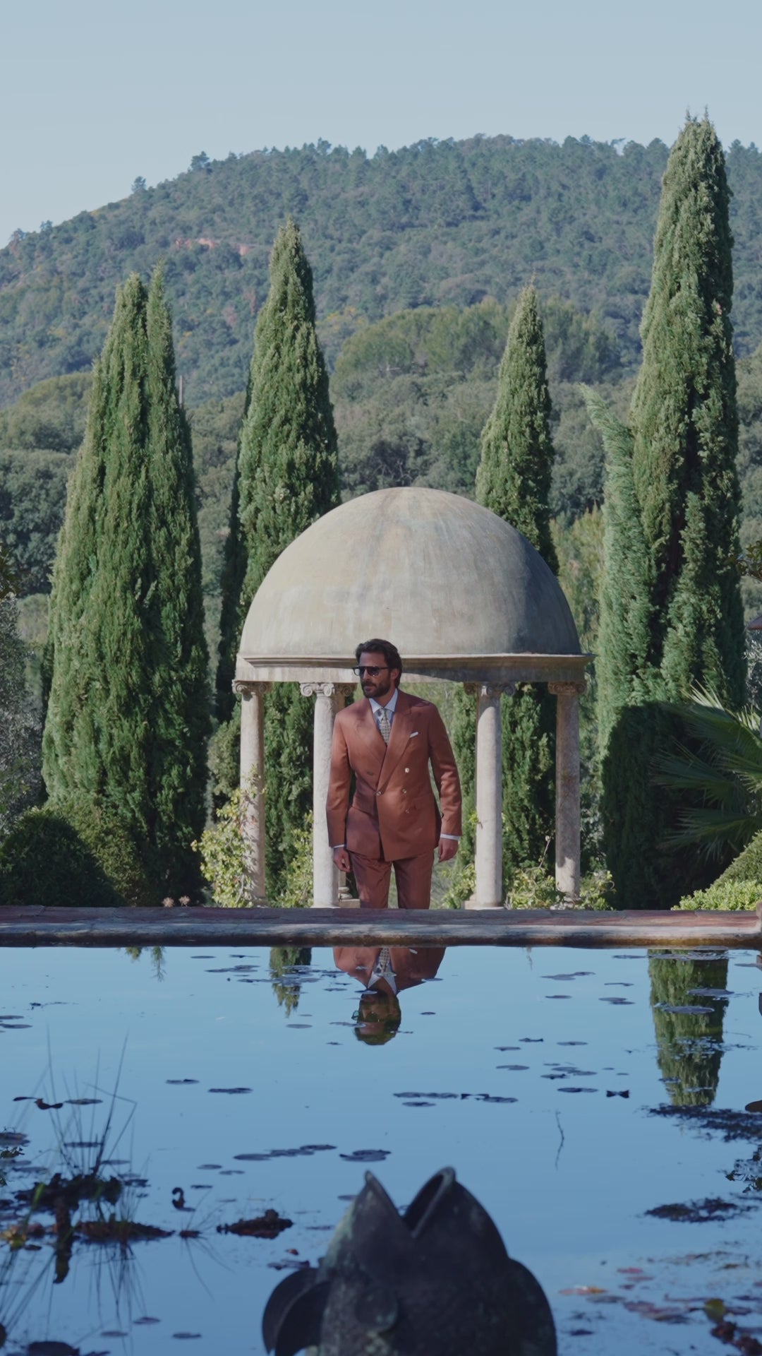 Men’s terracotta-toned suit reflected in a garden pool