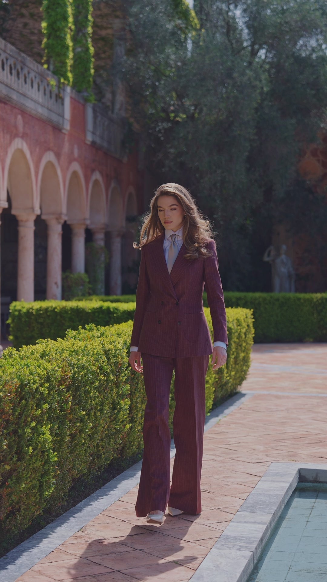 Women’s burgundy suit with wide-leg trousers on a garden path