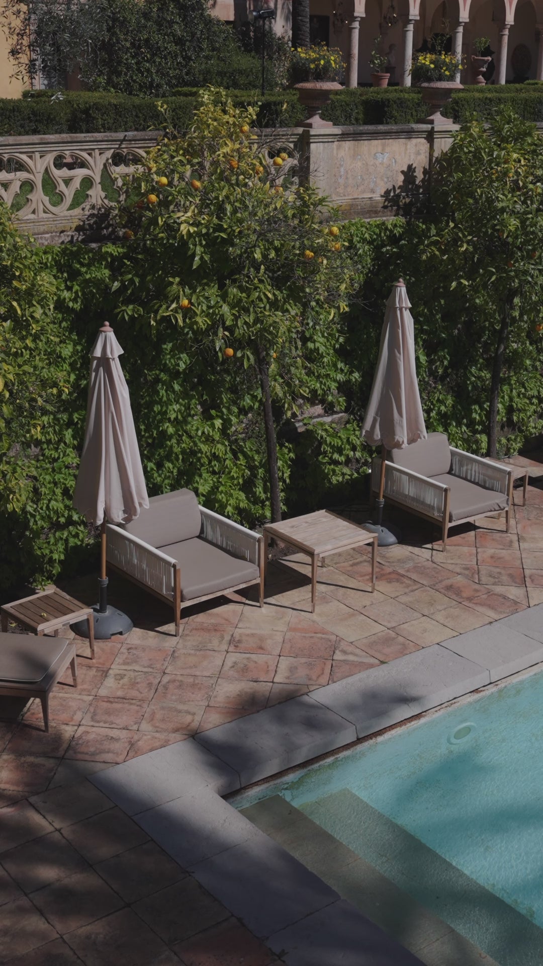 A turquoise pool with armchairs and parasols in a citrus garden