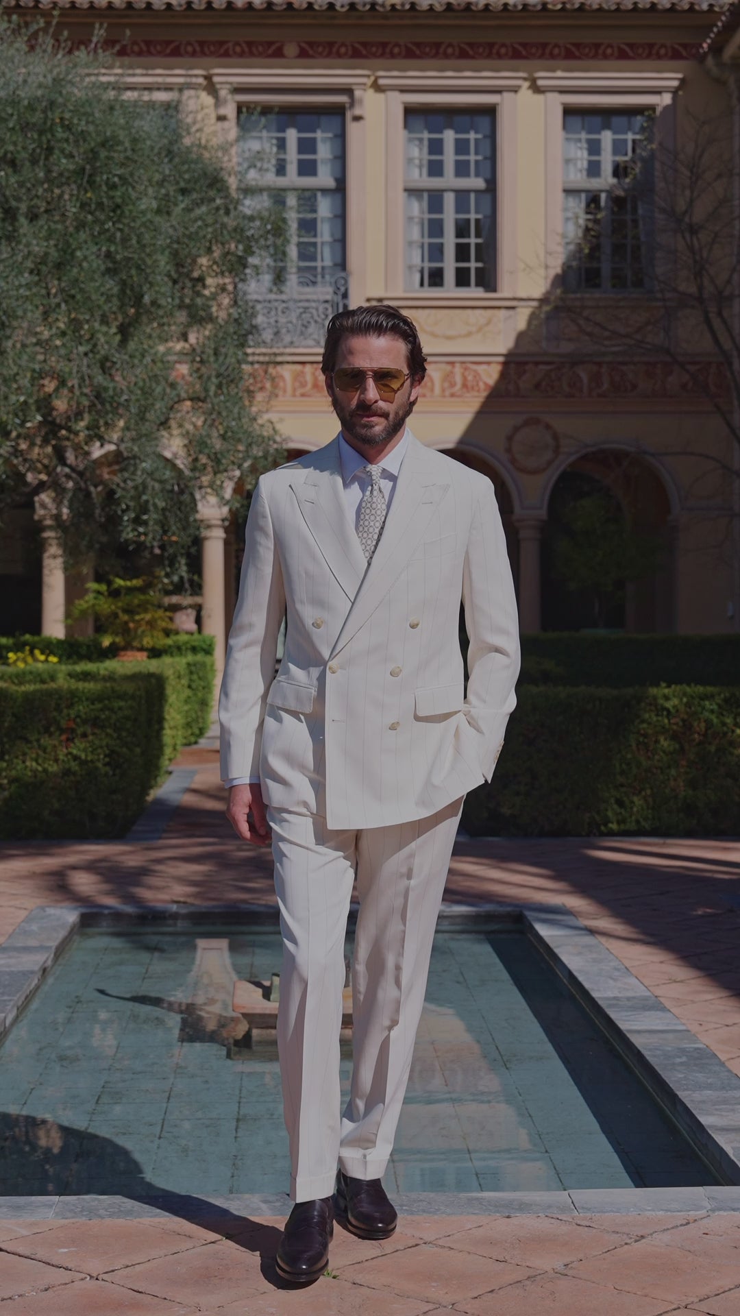 Men’s ivory double-breasted suit beside a garden pool