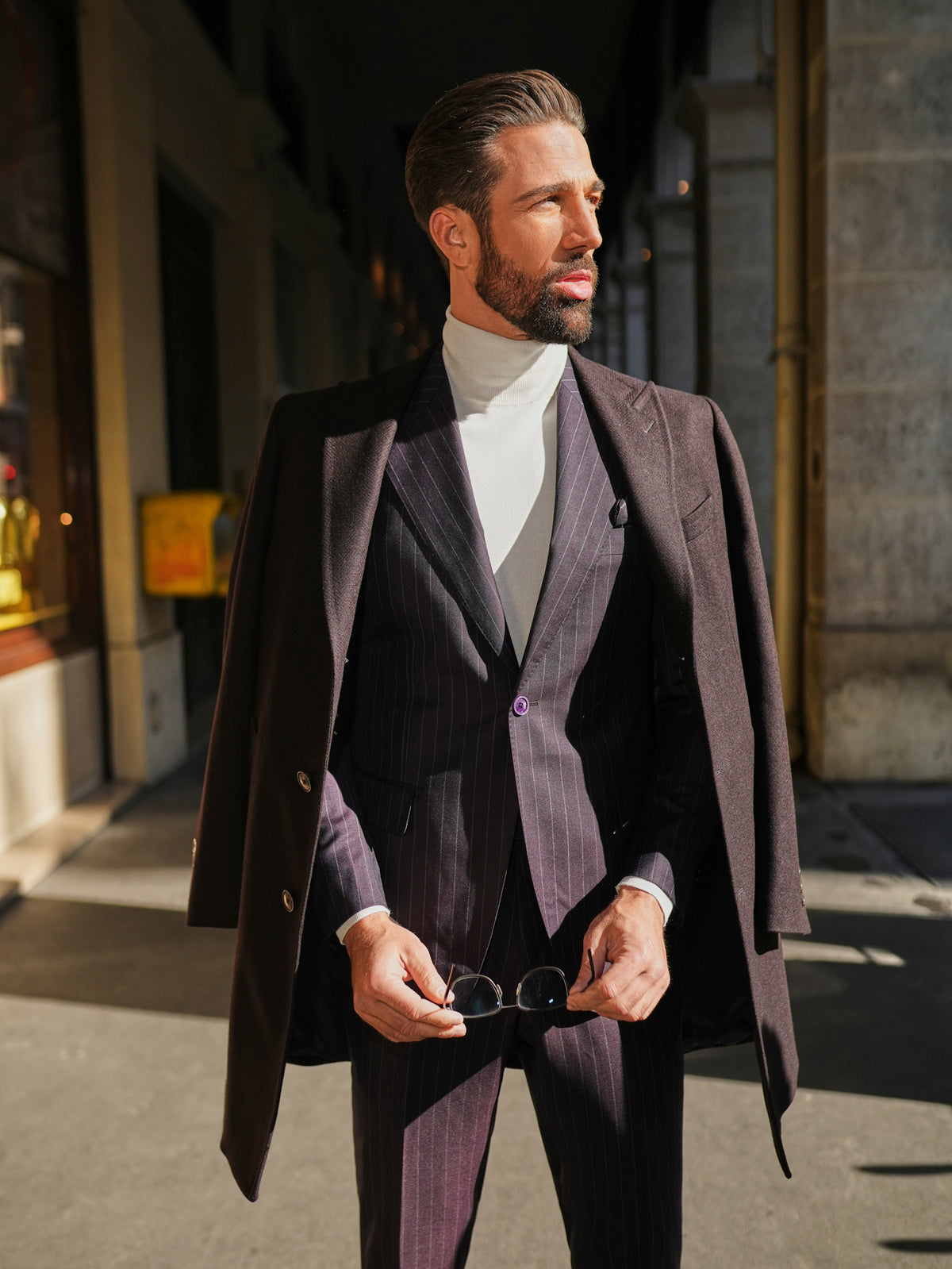 Consiglieri St Moritz: dark overcoat draped over a fine-striped suit